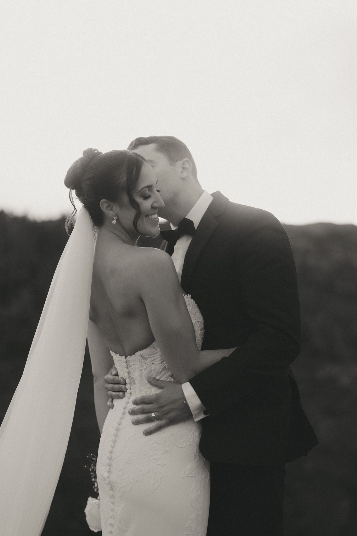 Black and white wedding photo of bride and groom sharing a tender kiss, bride in lace gown with veil.