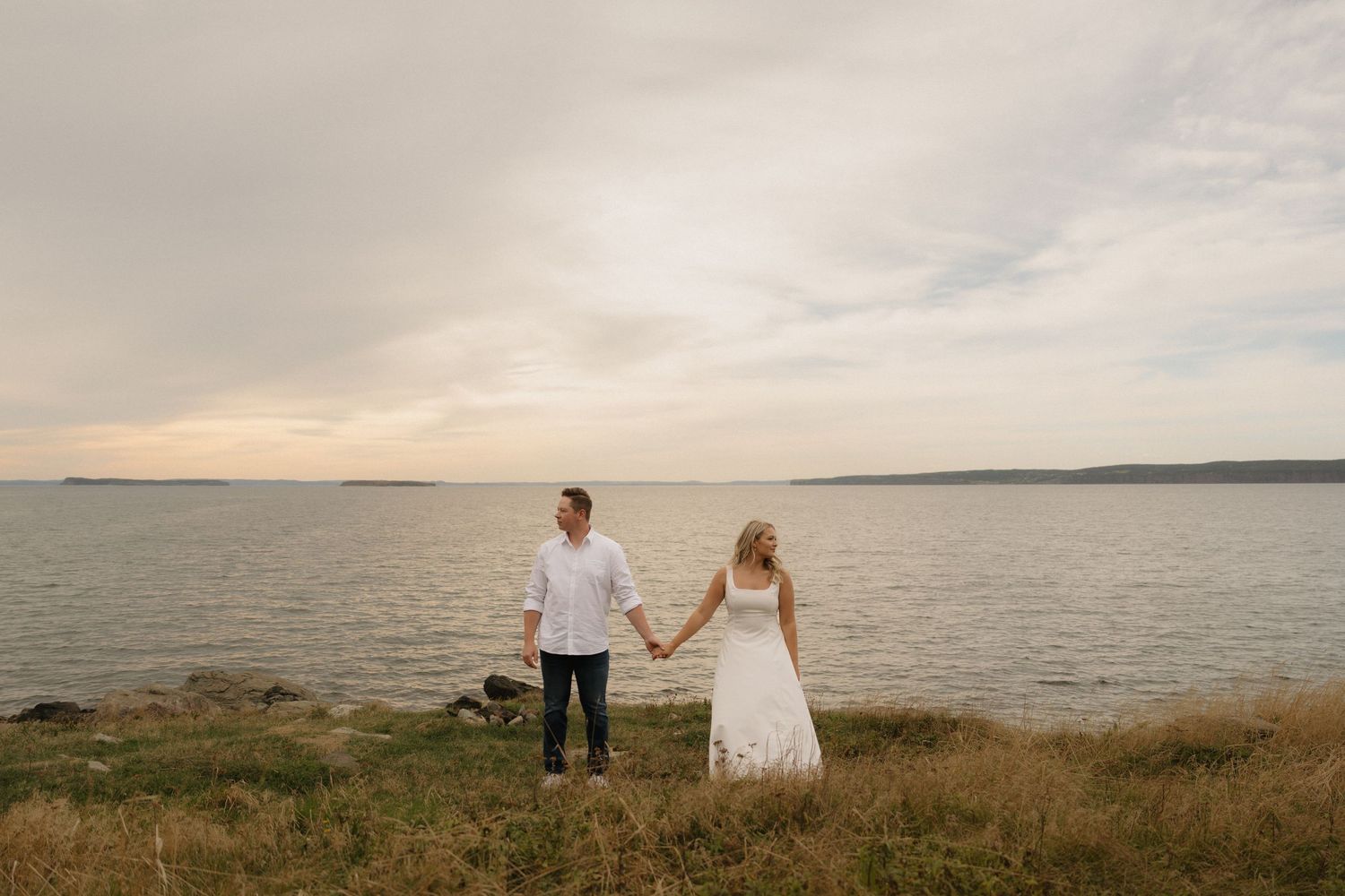 Panoramic view of a couple walking along a scenic coastal cliff at sunset.