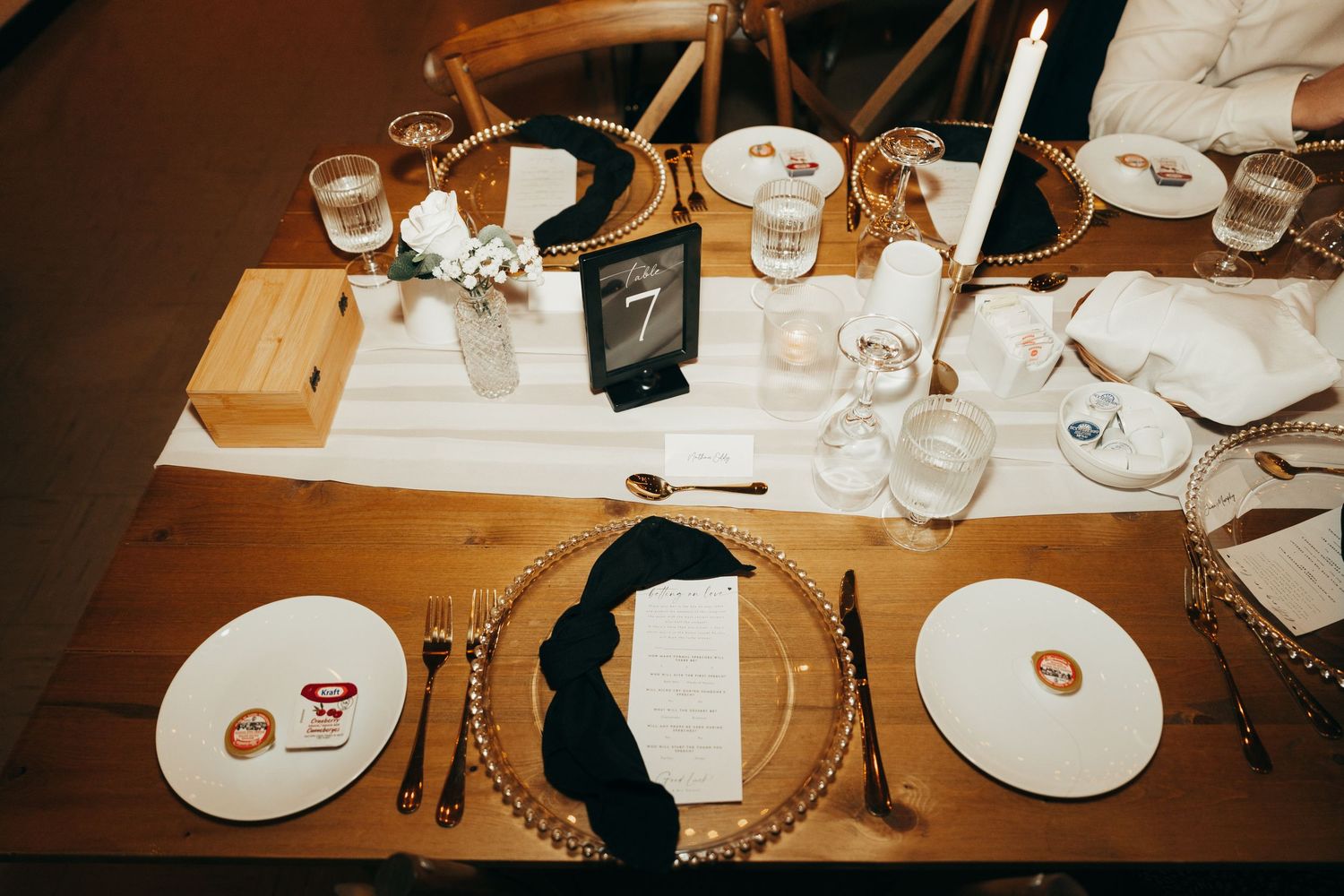 Elegant place settings with white plates and wine glasses on a wooden table at an upscale restaurant or event.