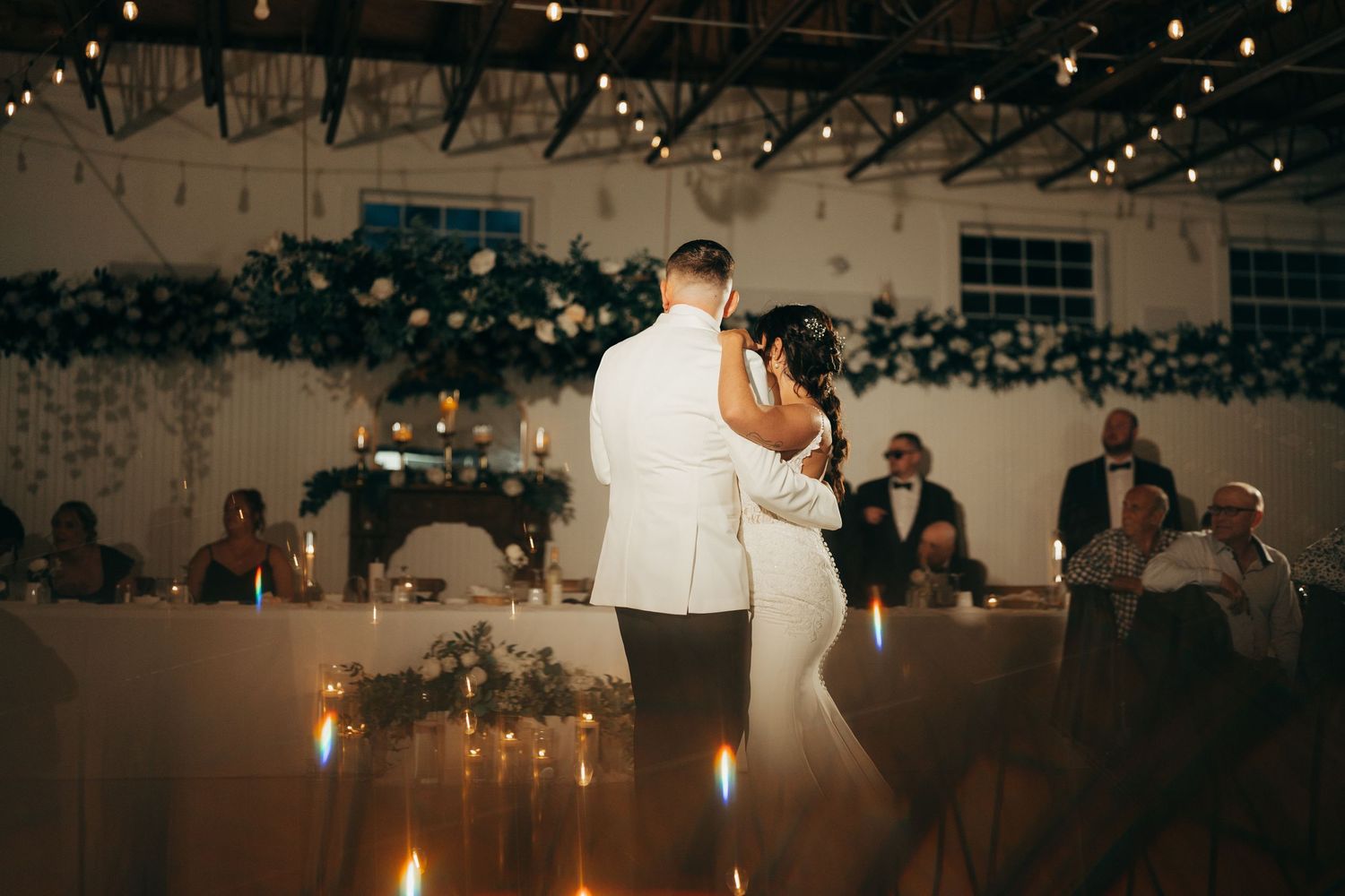 Couple shares their first dance at wedding reception with string lights and greenery decorating the venue.