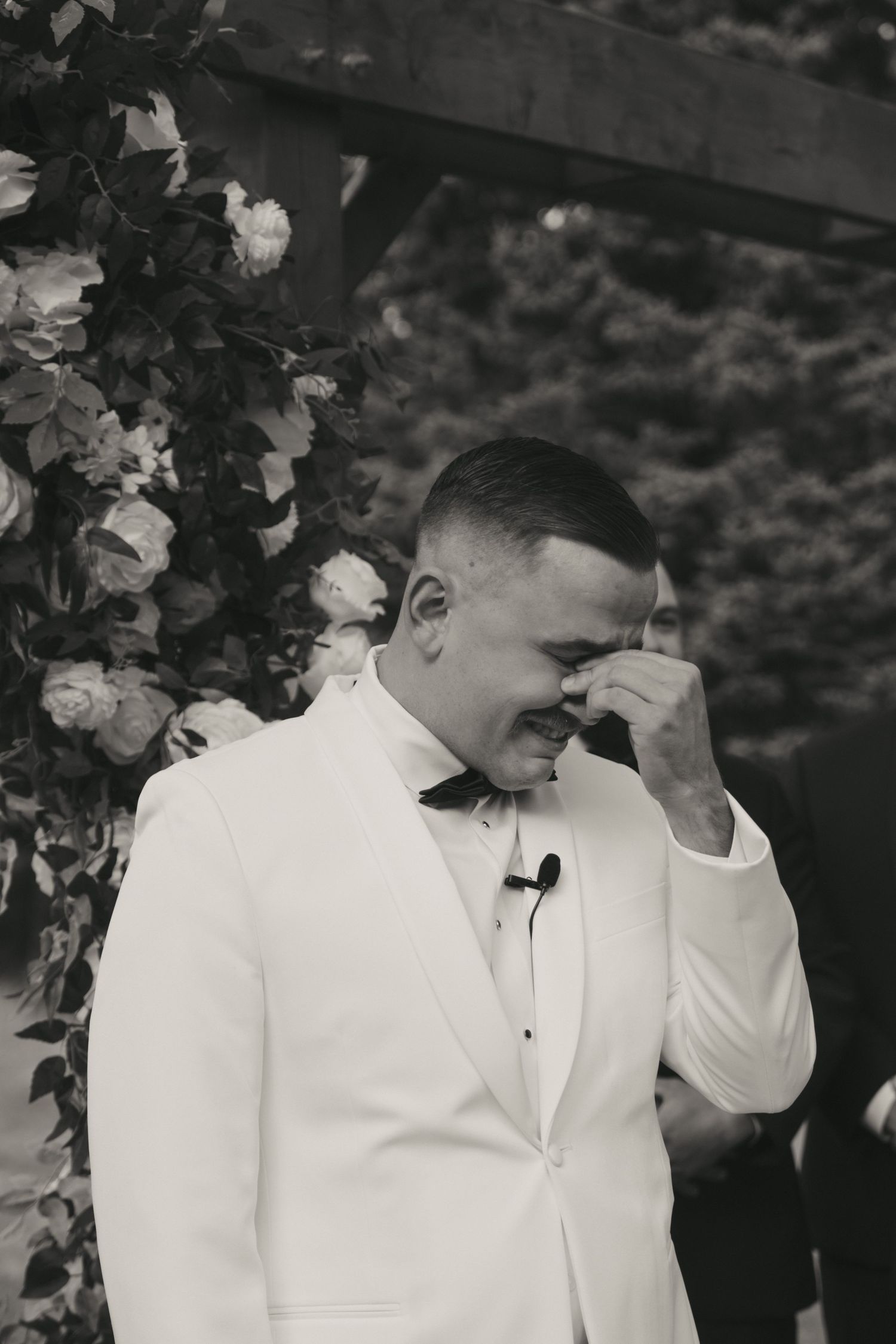 Black and white photo showing two people in white formal attire standing together in an intimate moment.