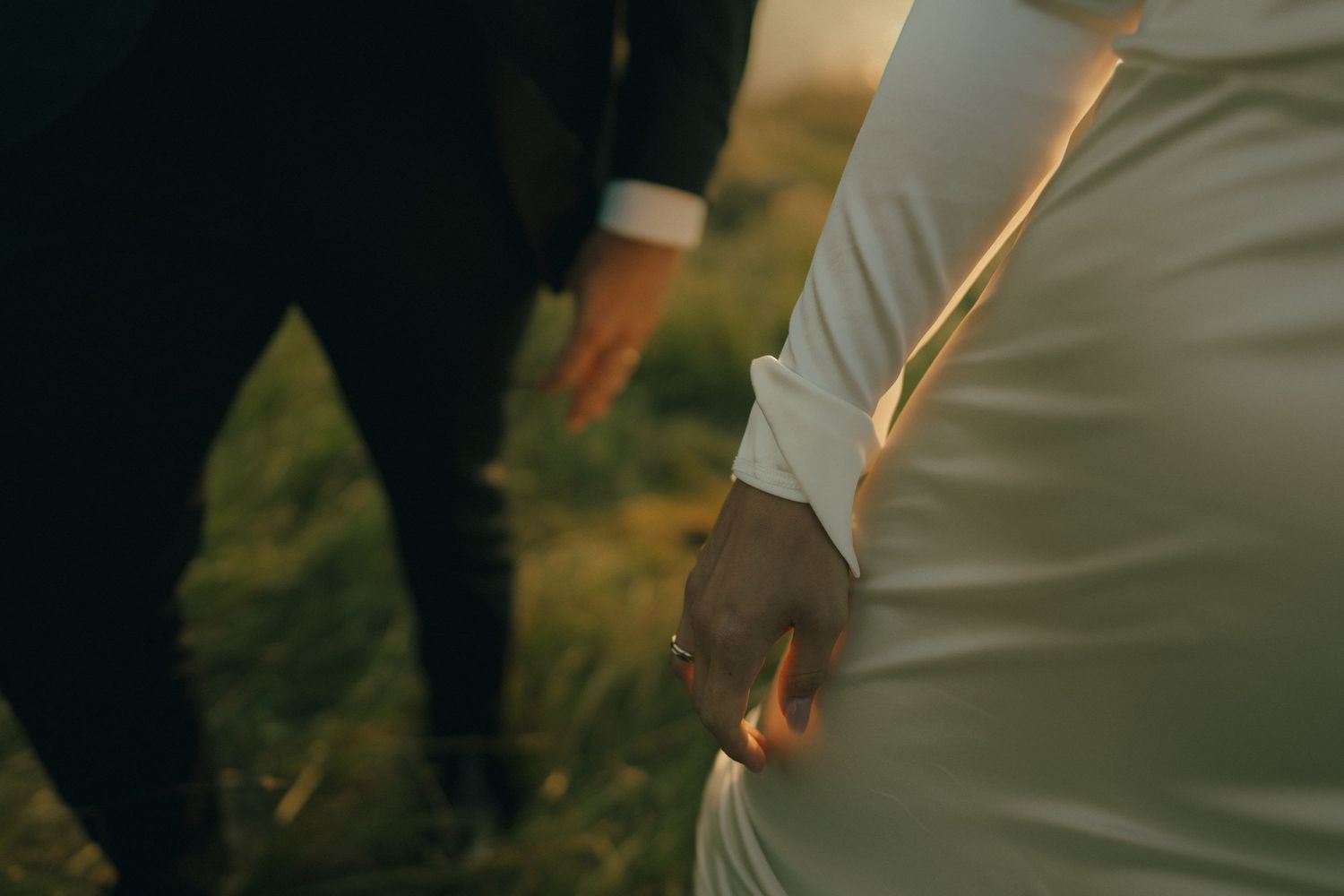 A couple holds hands during their wedding ceremony in a sunlit outdoor garden setting.
