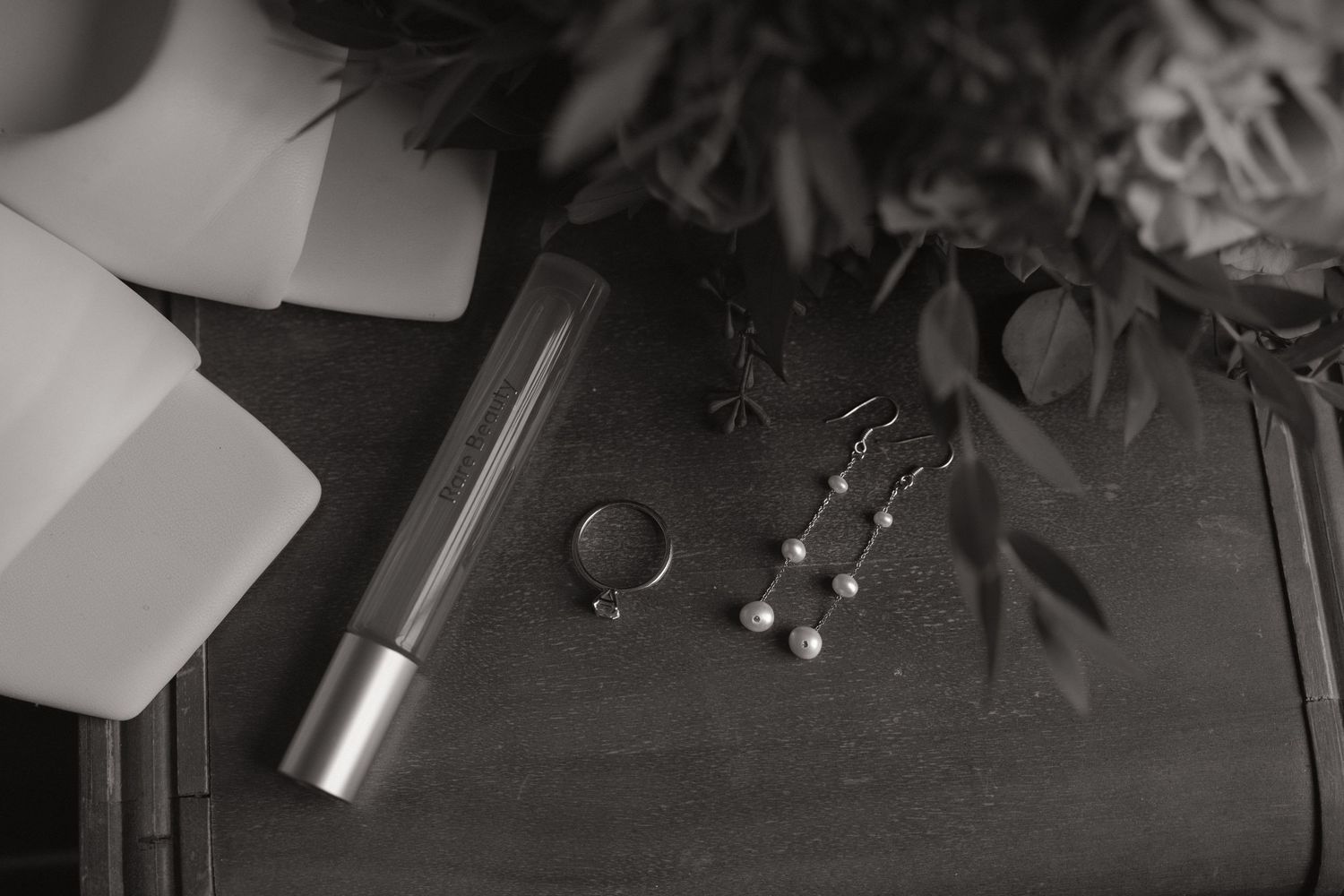 Black and white still life with lipstick, jewelry, and decorative elements on a dark surface.