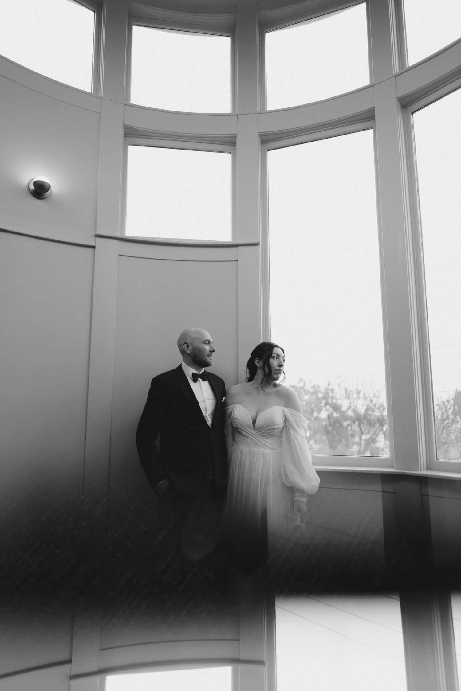 Black and white artistic wedding photo series showing a couple in an elegant curved window setting with natural light.