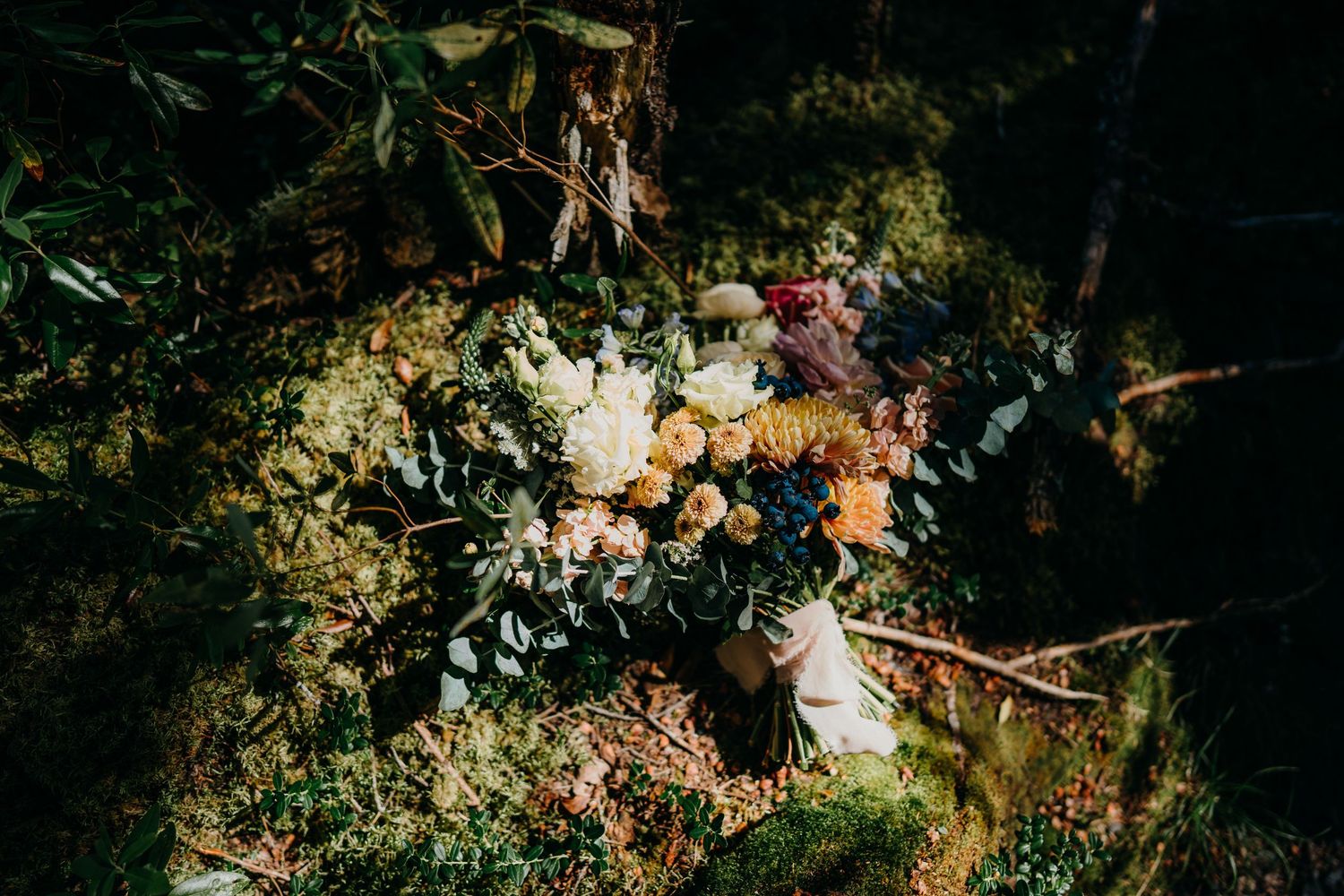 Moody floral arrangement with mixed blooms in dramatic lighting against dark background.