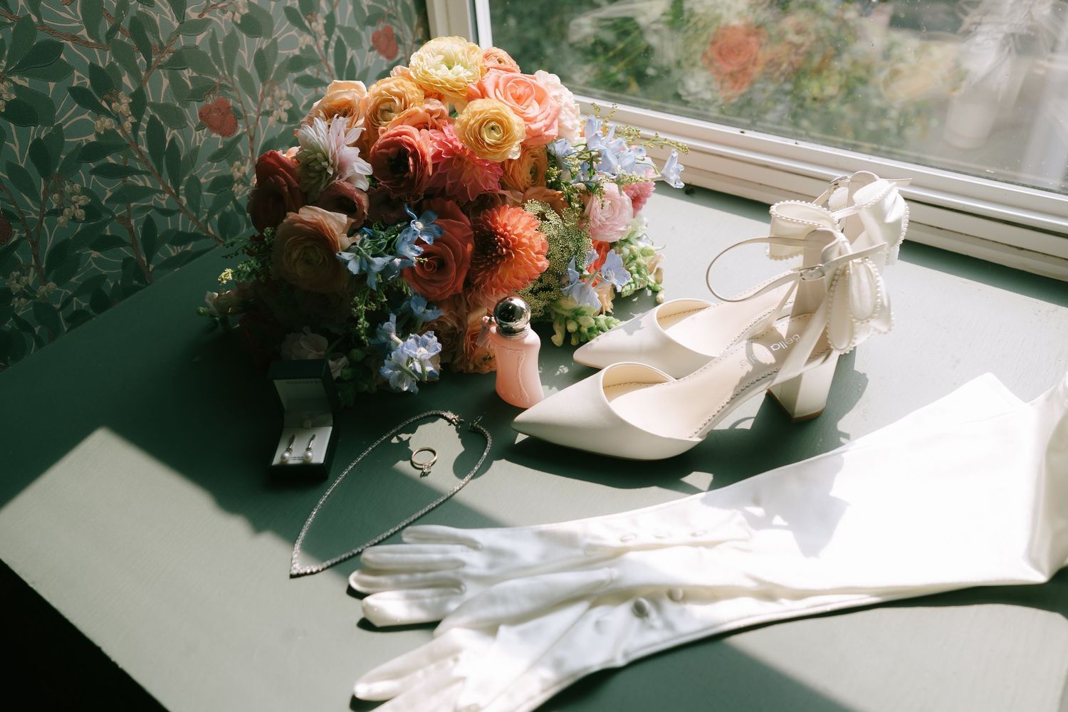 Wedding details with peach flowers and white shoes arranged artistically in natural light.