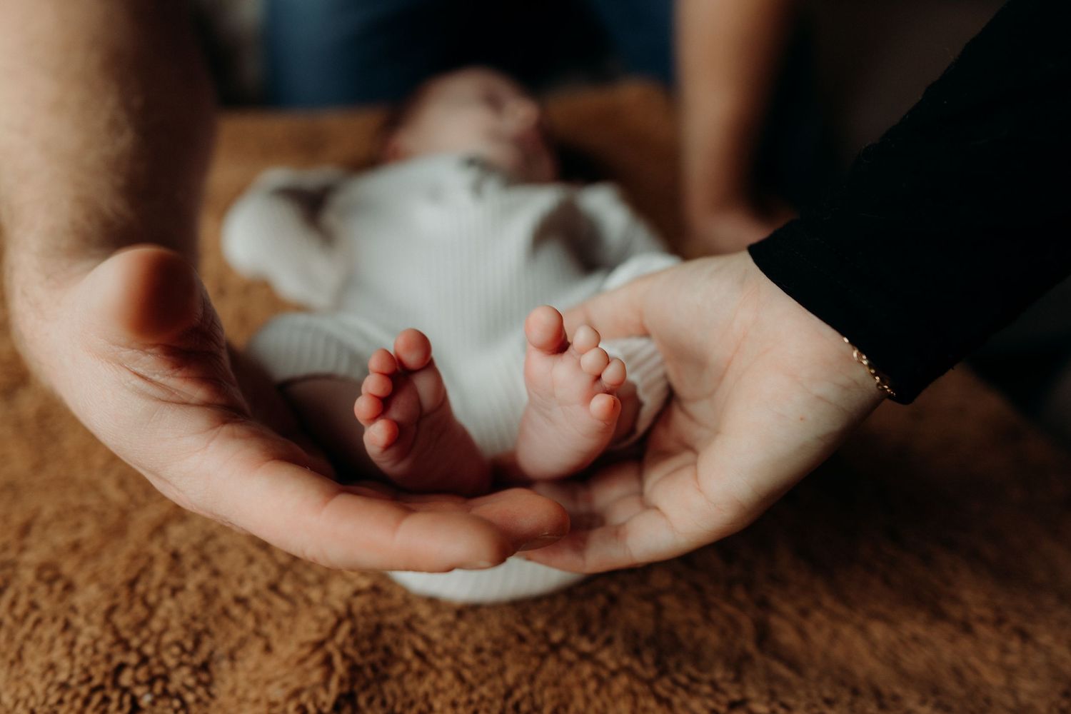 Close up view of tiny newborn fingers being gently held against a warm brown textured background.