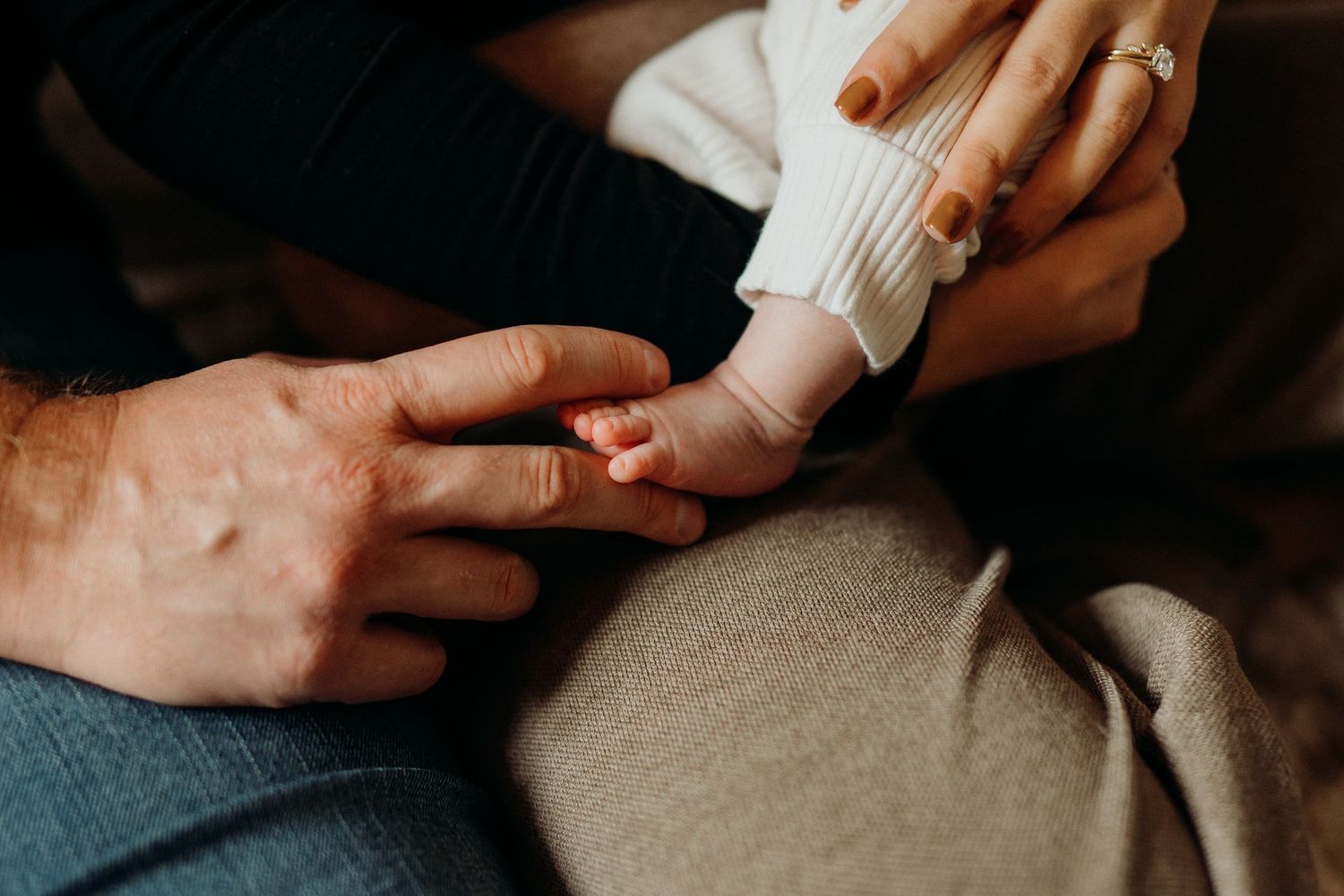 Baby in a white sweater being held while resting on a patterned rug in moody lighting.