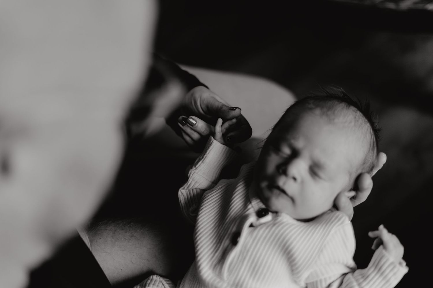 Intimate black and white portrait of a family bonding with their newborn in a cozy living room setting.