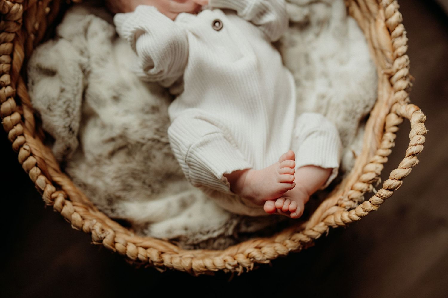 High angle view of baby resting in circular woven bassinet with white bedding.