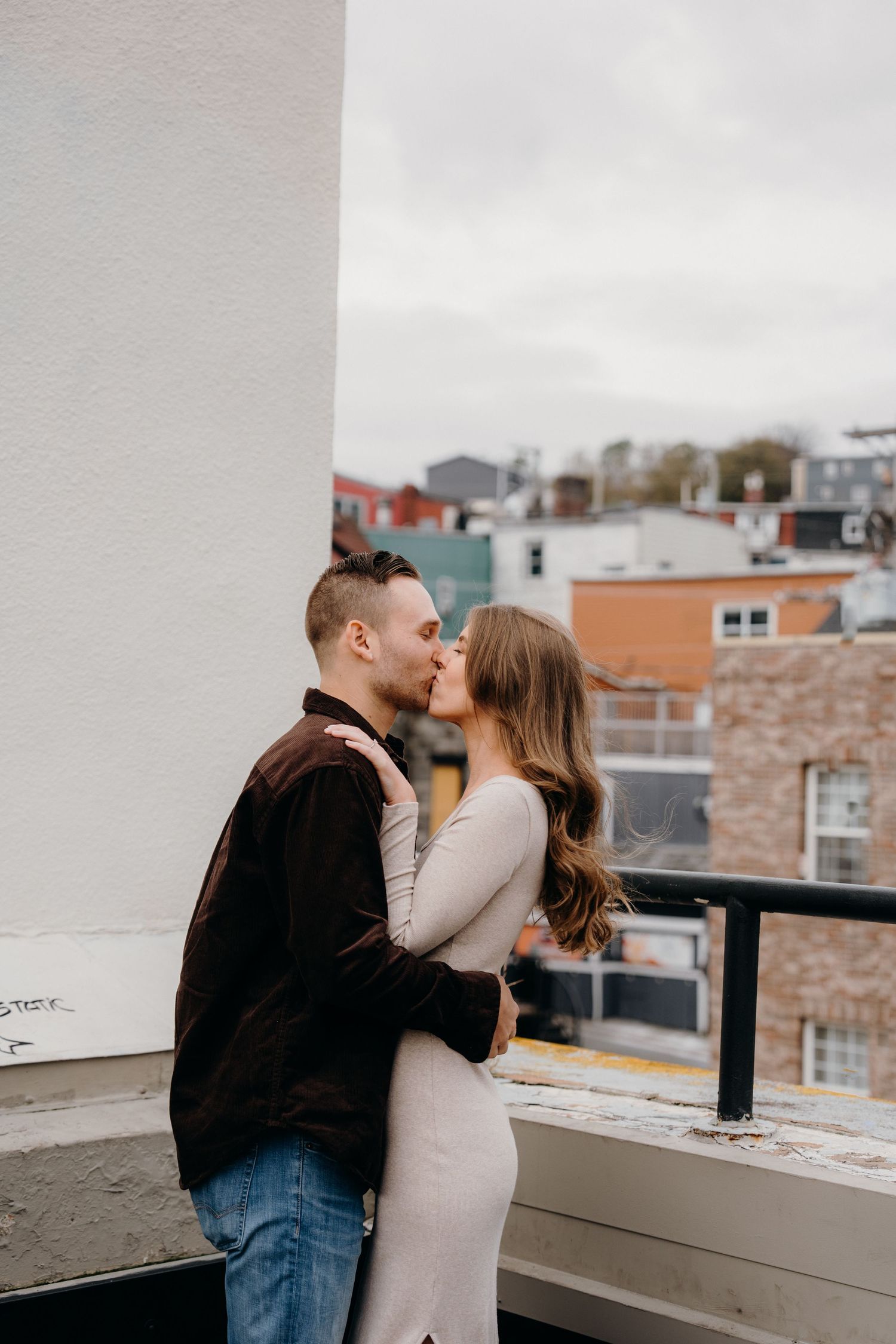 A romantic moment between a couple on an urban rooftop with city buildings in the backdrop.