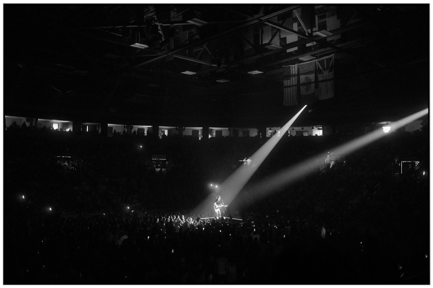 Concert crowd illuminated by bright spotlights during a live performance in a dark arena.