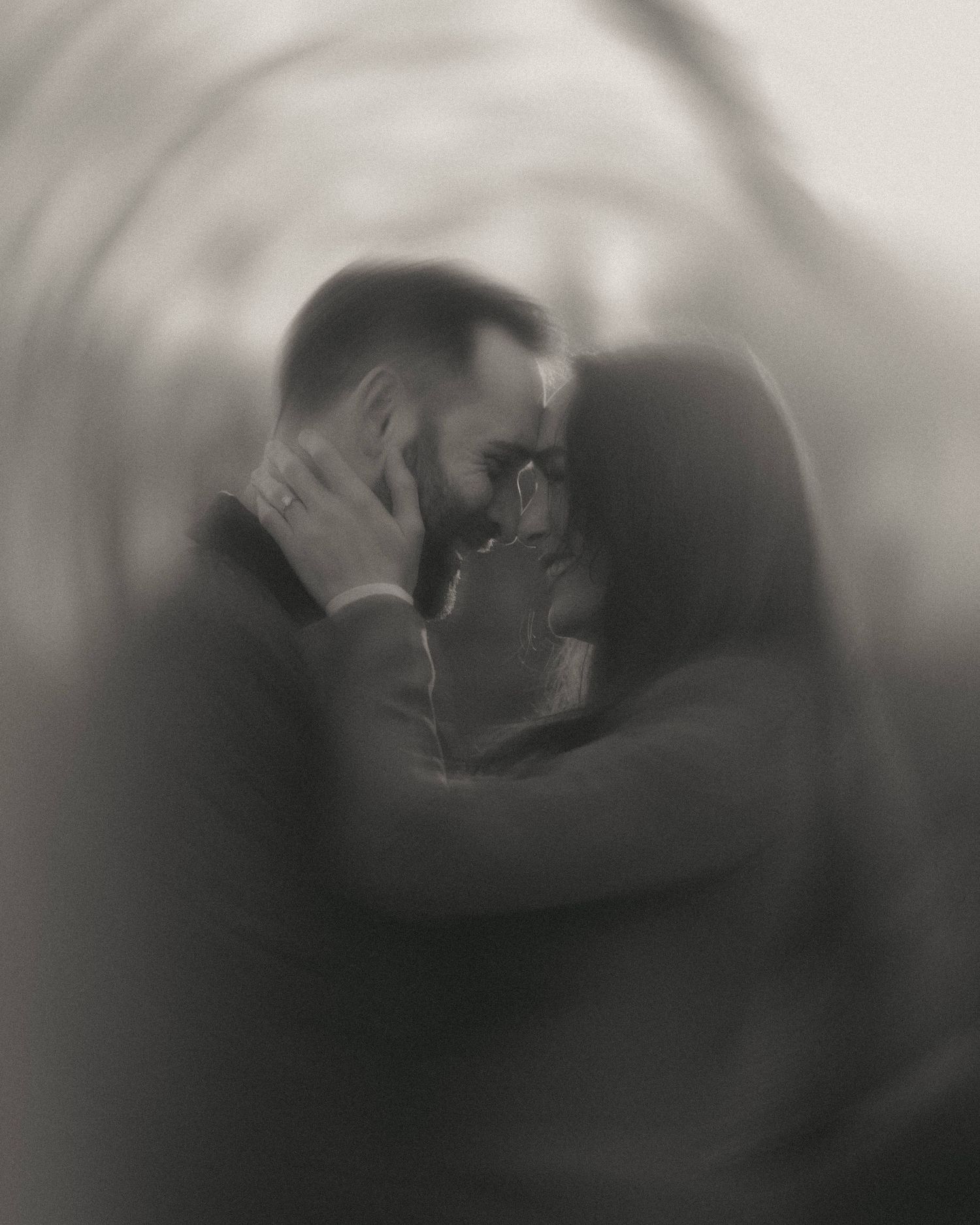 Black and white blurred photo of a romantic couple embracing closely, forehead to forehead, in a dreamy swirl effect.