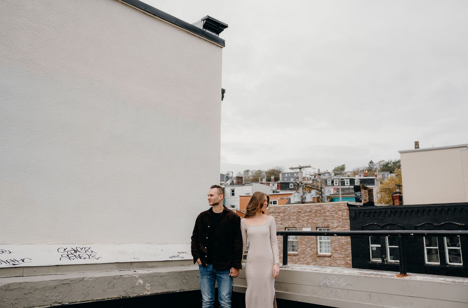 A rooftop view of an urban neighborhood with brick buildings and white walls against an overcast sky.