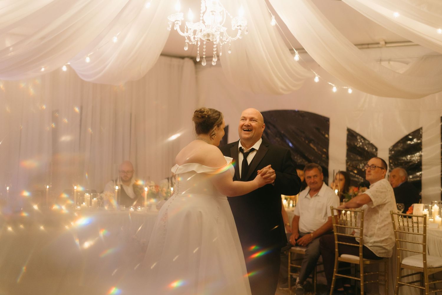 Wedding reception featuring romantic dancing beneath elegant white draping and string lights.