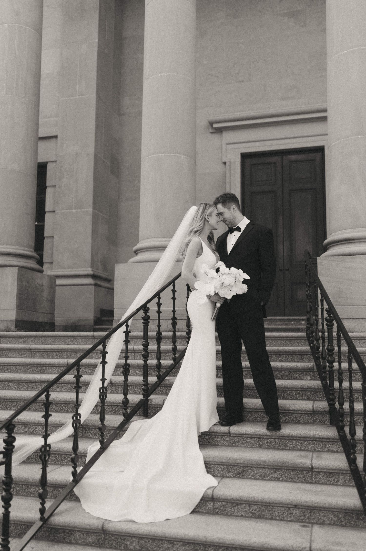 Wedding couple poses romantically on steps of classical building with columns.