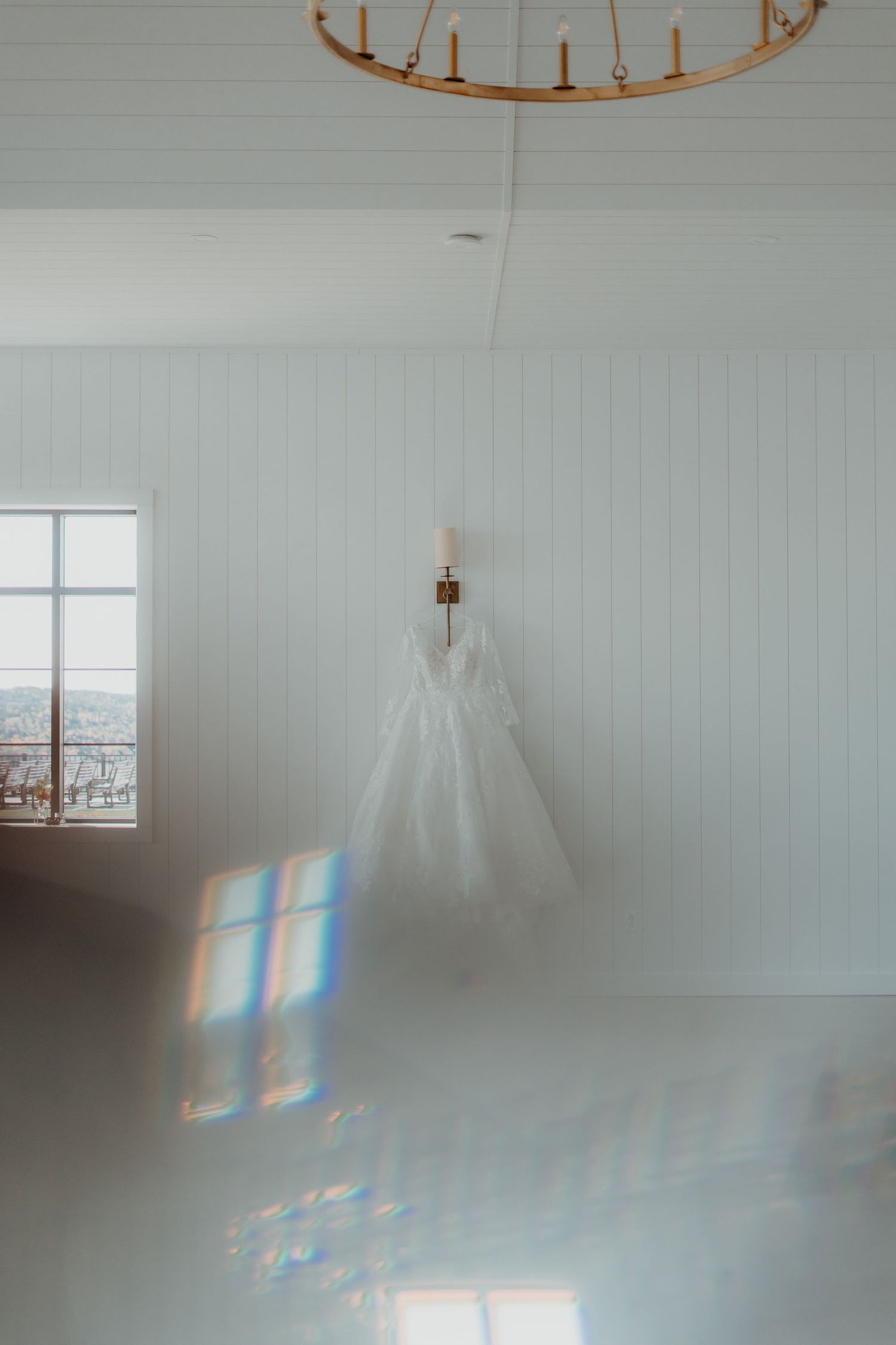 Minimalist white room with hanging chandelier and wedding dress creating ethereal light patterns.