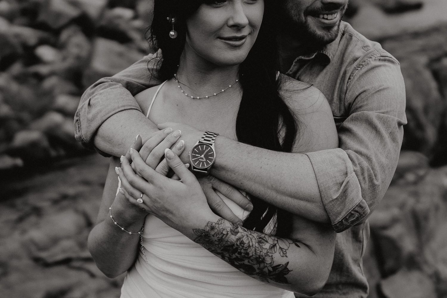 A couple shares laughter while embracing on rocky coastal terrain.