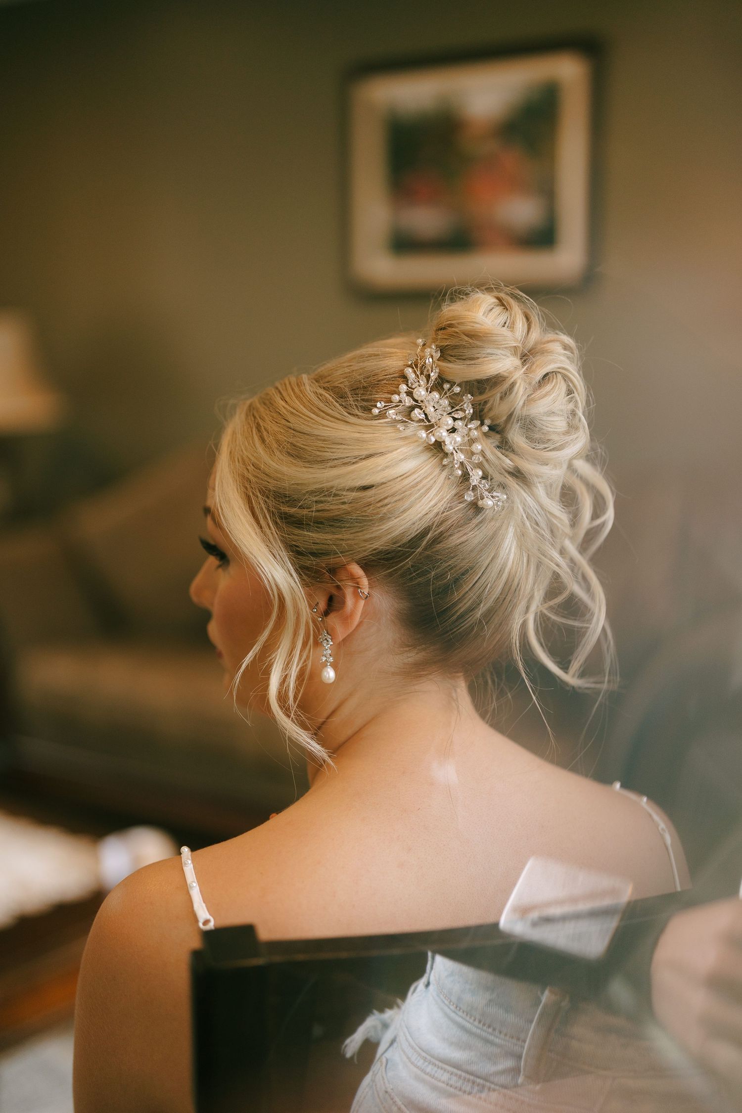 Elegant bridal updo with crystal hair accessory and pearl drop earring on blonde hair.