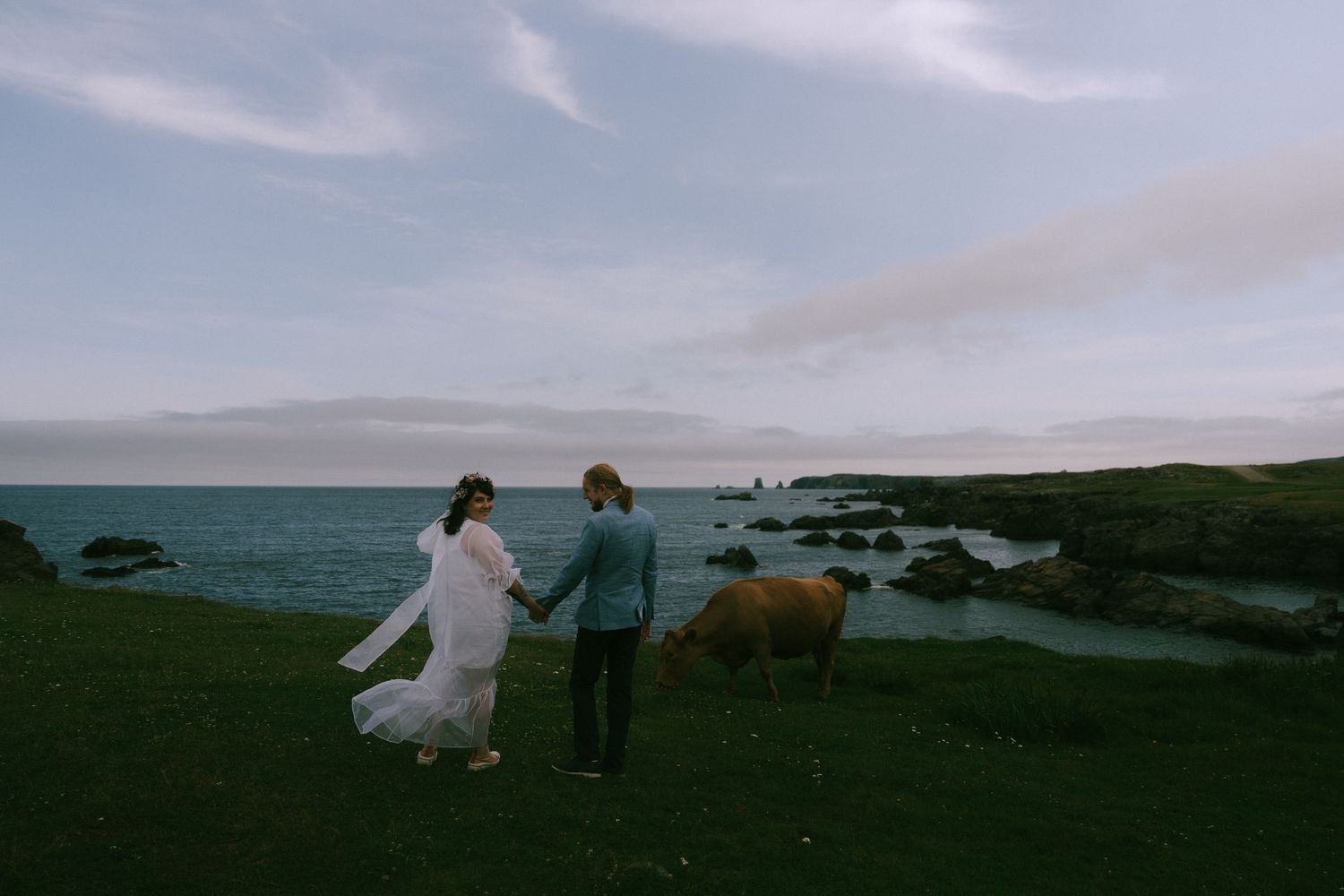 Silhouettes of people exploring a dramatic coastal landscape at dusk with rocky cliffs and ocean views.