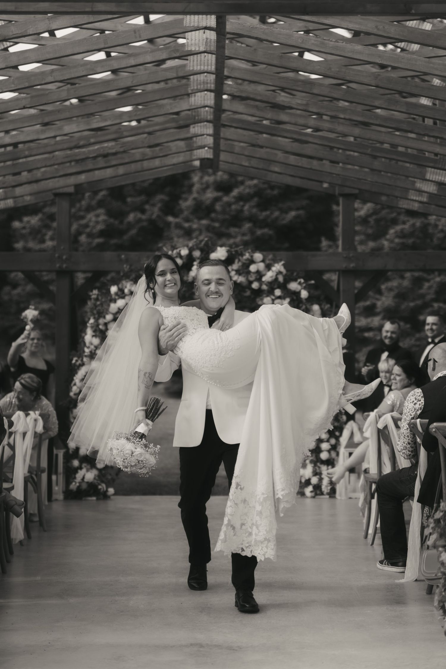 Couples dancing in formal attire at a ballroom event with white gowns and tuxedos under a vaulted ceiling.