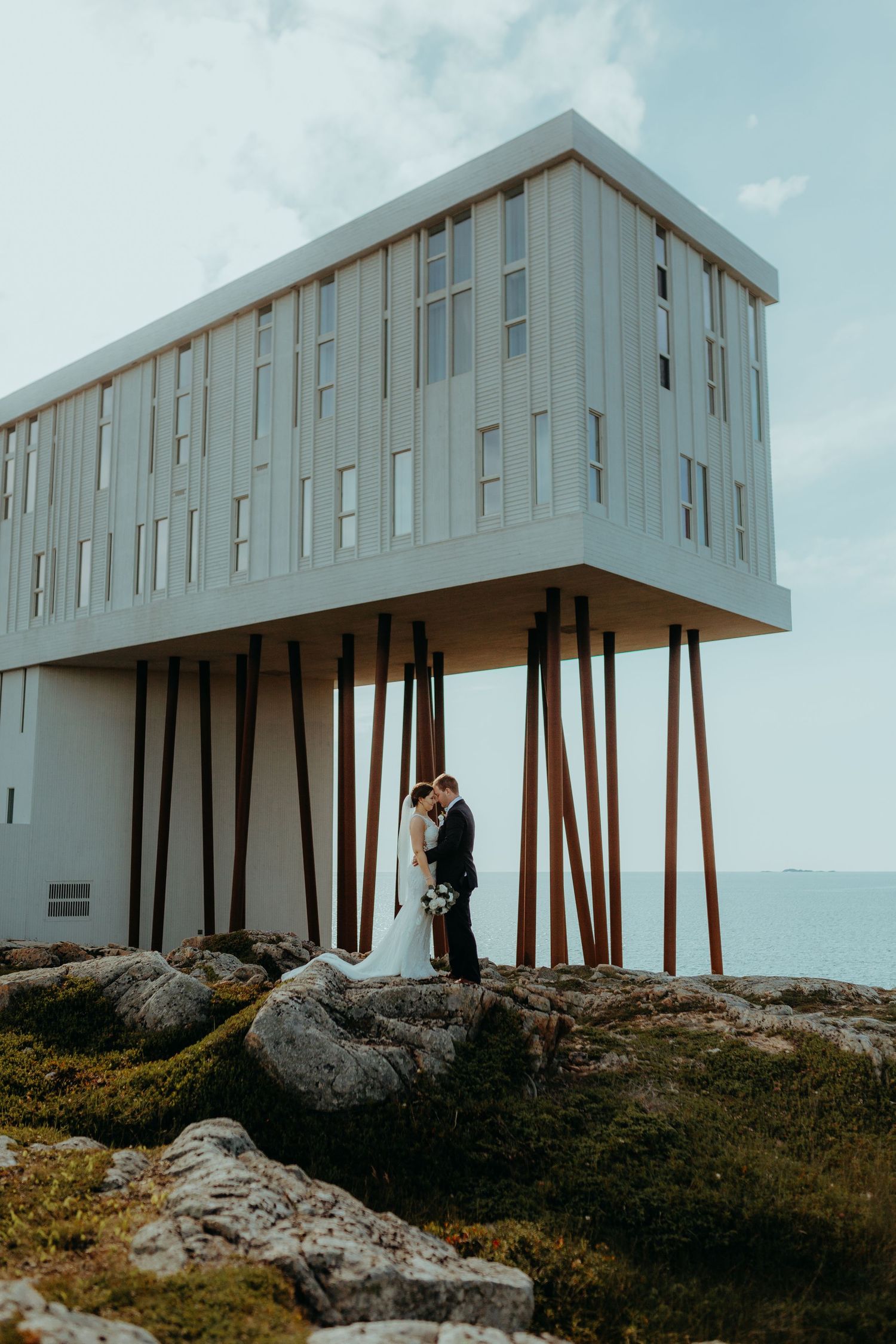 Modern architectural wedding venue perched on stilts against a cloudy sky.