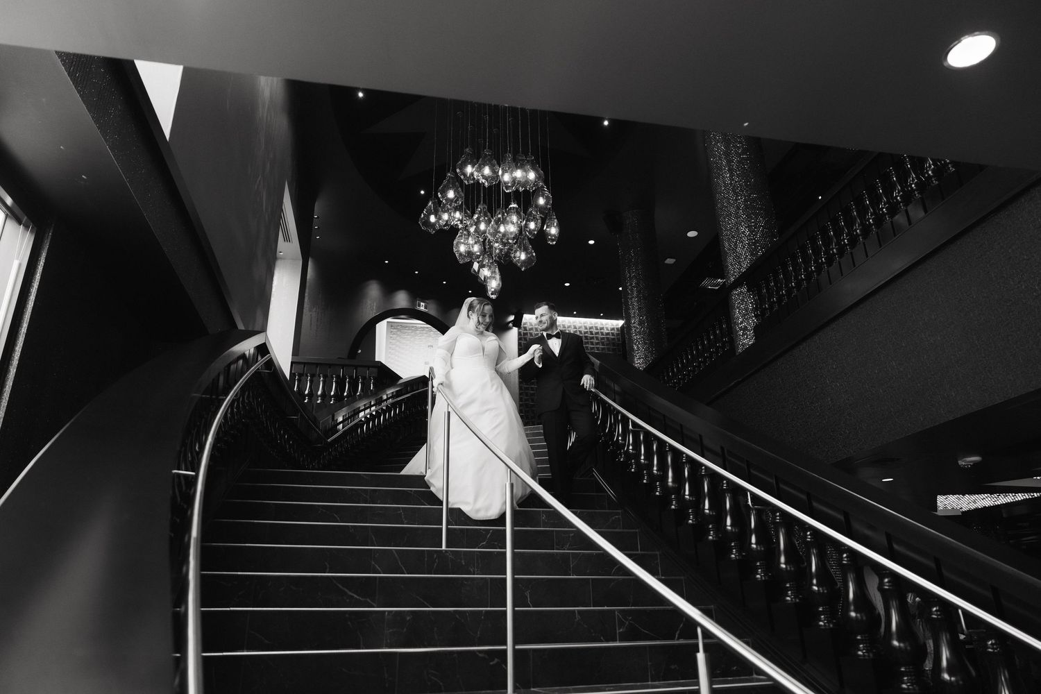 Black and white wedding photo captures dramatic shadows and lines along an elegant modern staircase.