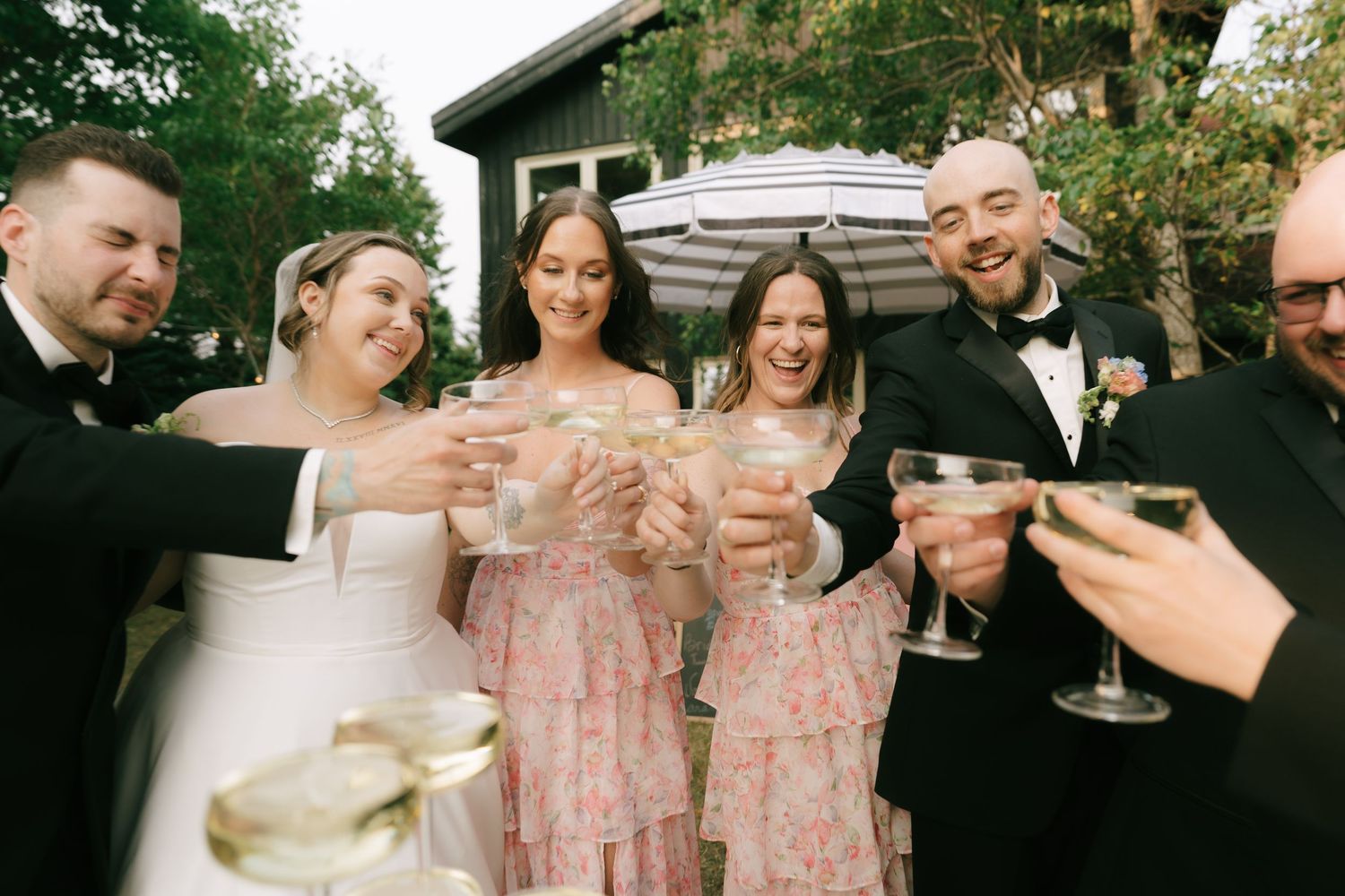 Wedding party gathers for a celebratory toast under a striped umbrella.