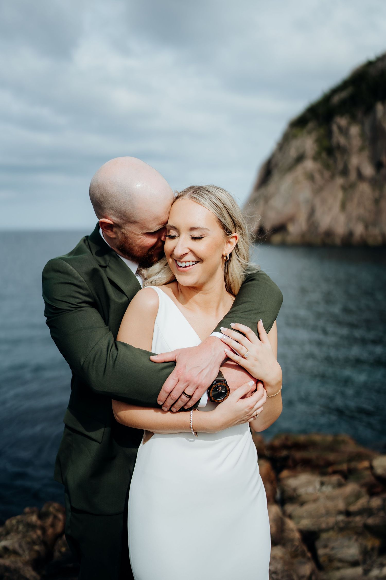 Tender embrace captured during seaside wedding shoot with rocky cliffs and ocean views.