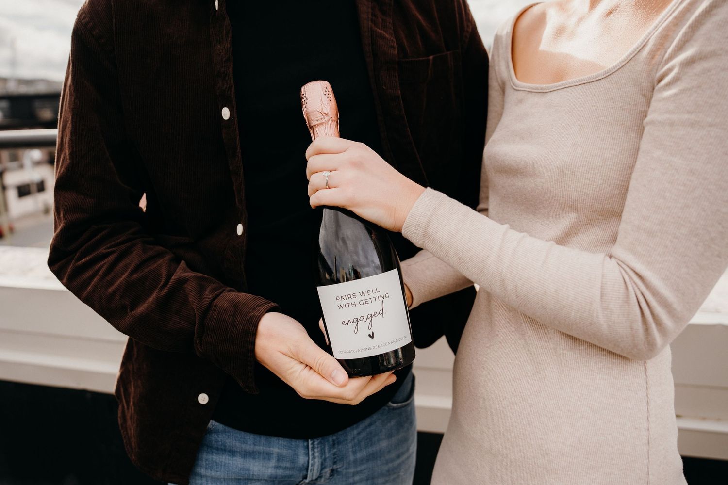 Hands exchanging a celebratory bottle of champagne against dark clothing.
