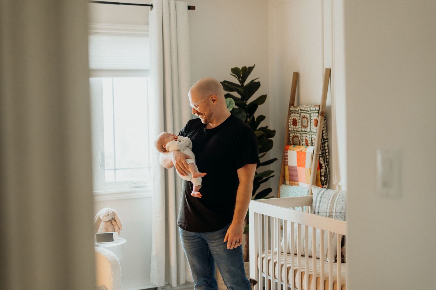 Person holding infant while standing in modern nursery with white furniture.