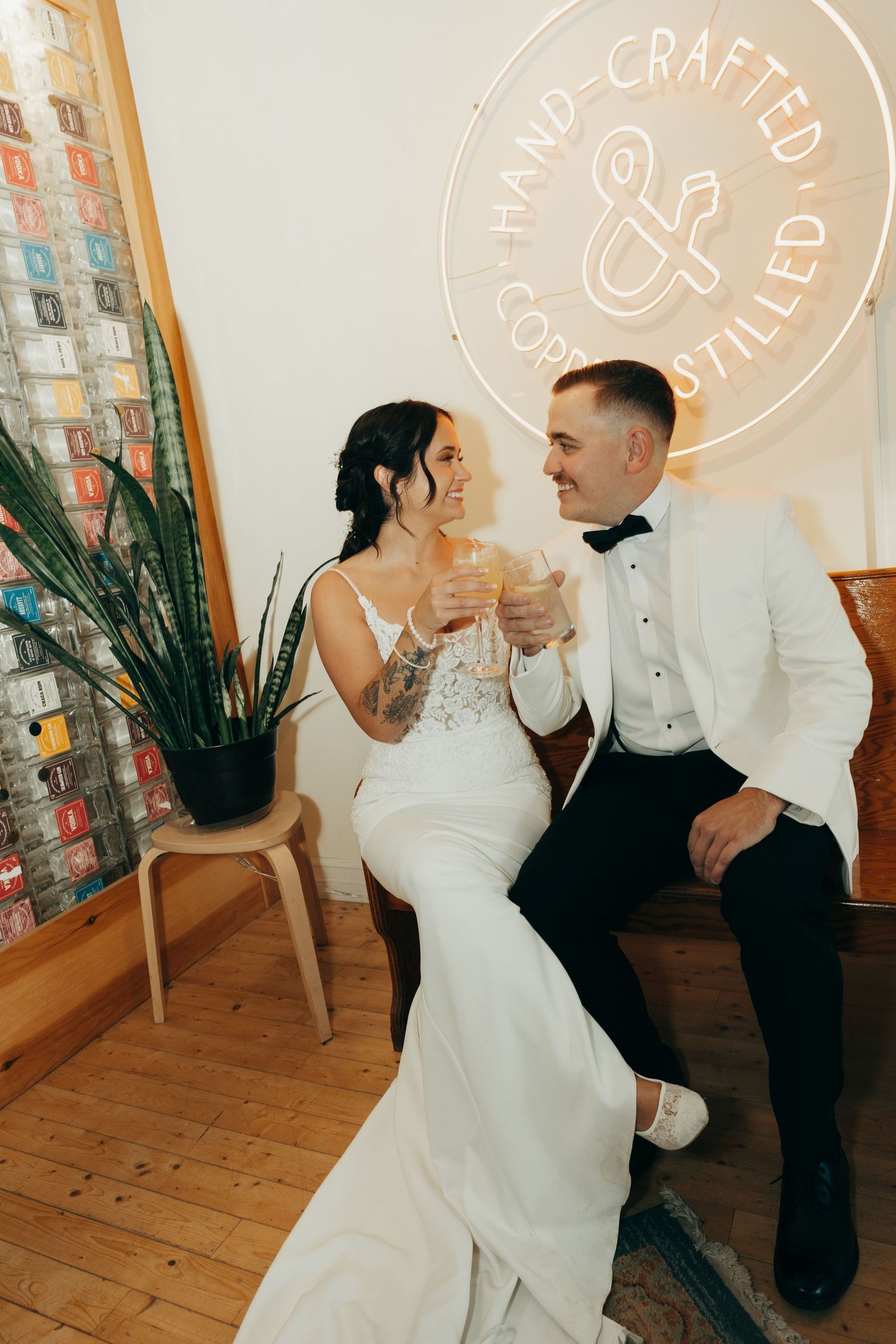 Dancing couple in wedding attire share intimate moments at an indoor venue with a rustic wooden floor and neon signage.