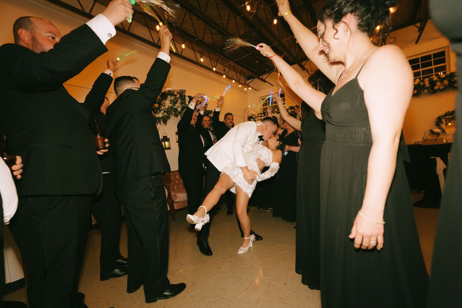 People dance together in formal attire at an evening reception with twinkling lights in the background.