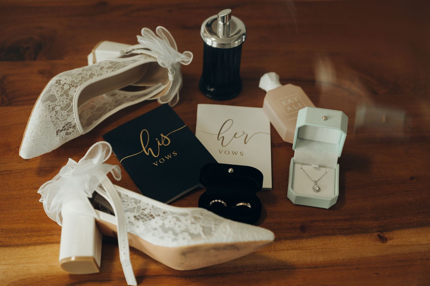 Wedding accessories including rings, jewelry boxes, and bridal shoes arranged on a dark wooden surface.
