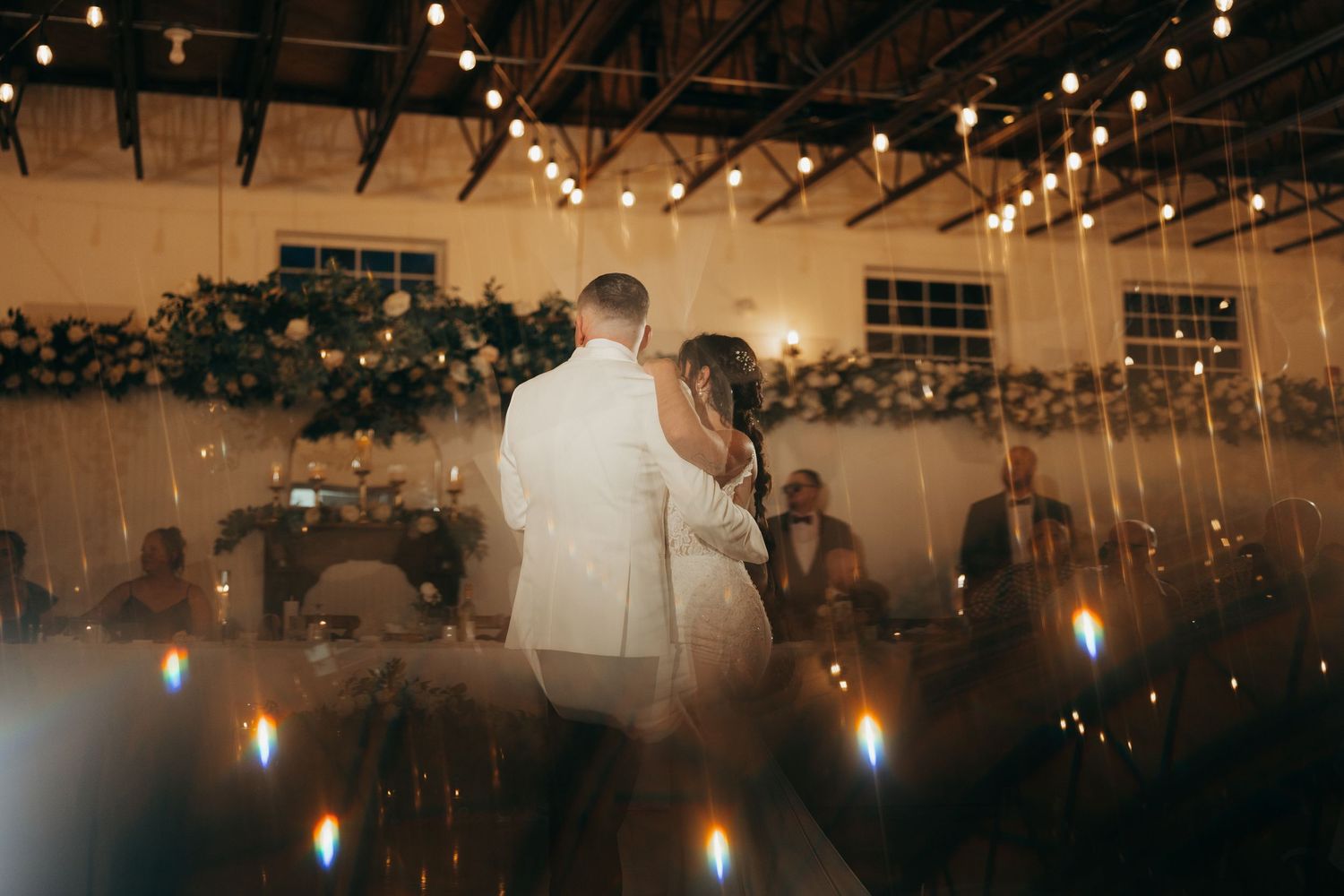 String lights create a warm ambiance at an evening wedding reception venue with rustic decor.