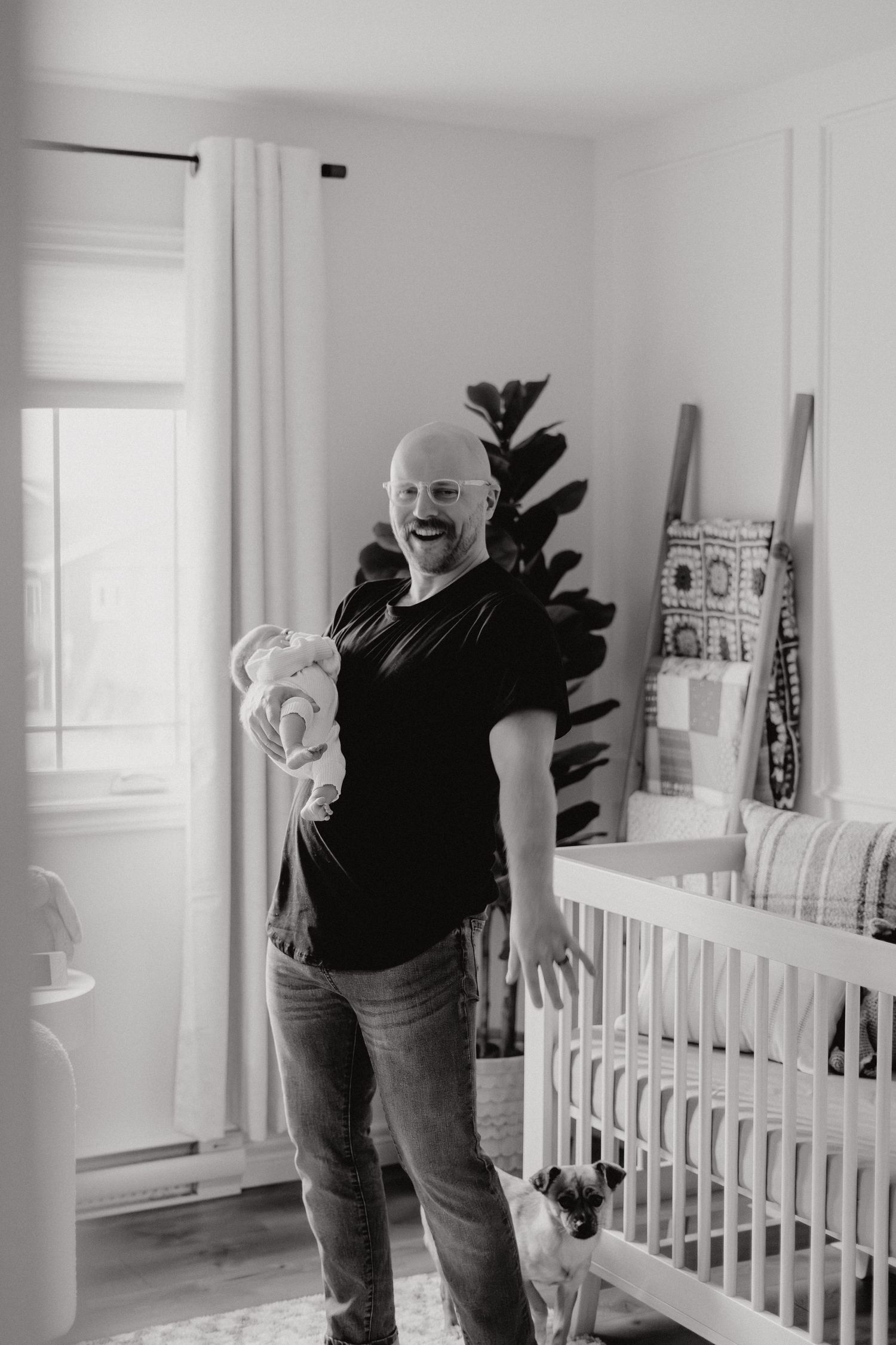 Person in black shirt holding infant while standing beside white crib in modern nursery.