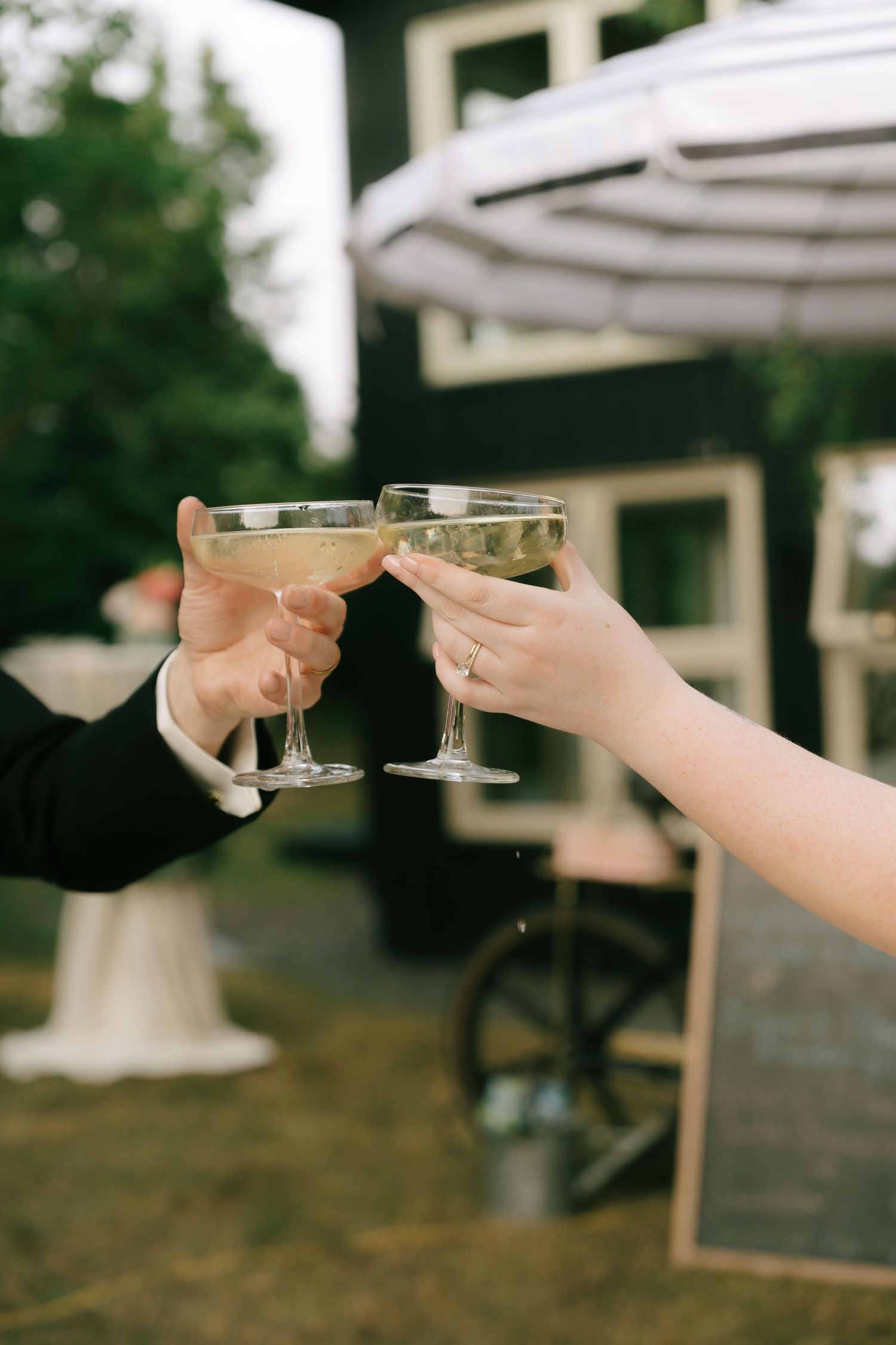 Two hands clink champagne glasses in a celebratory toast under a white umbrella.