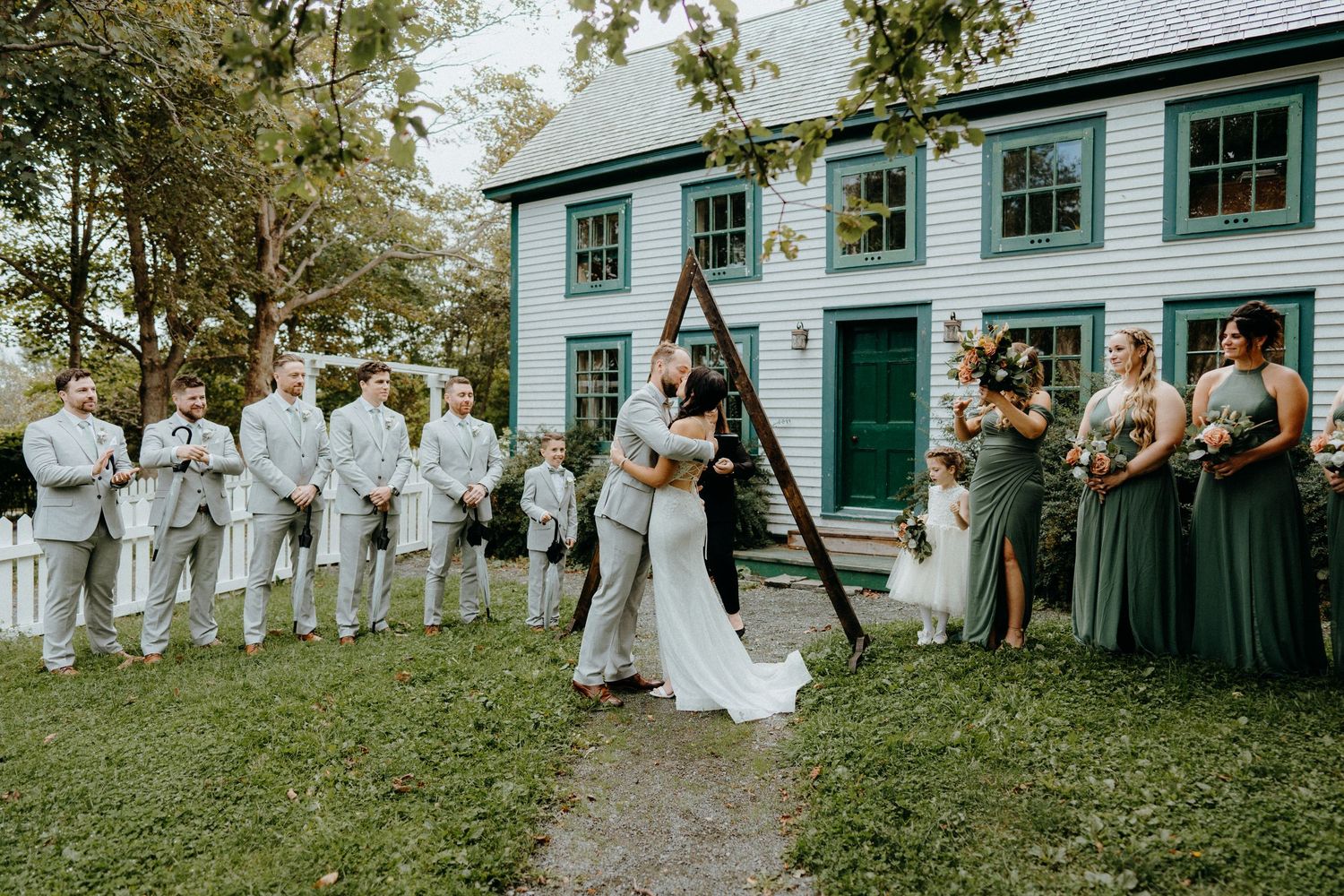 Wedding ceremony in front of historic green building with wedding party in sage green dresses.