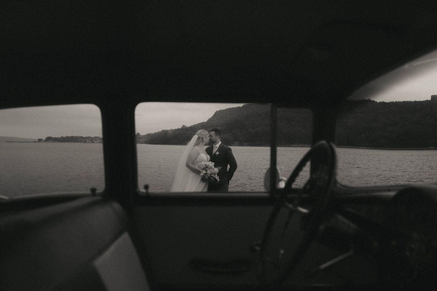 Black and white scenic landscape viewed through silhouetted car window frame.