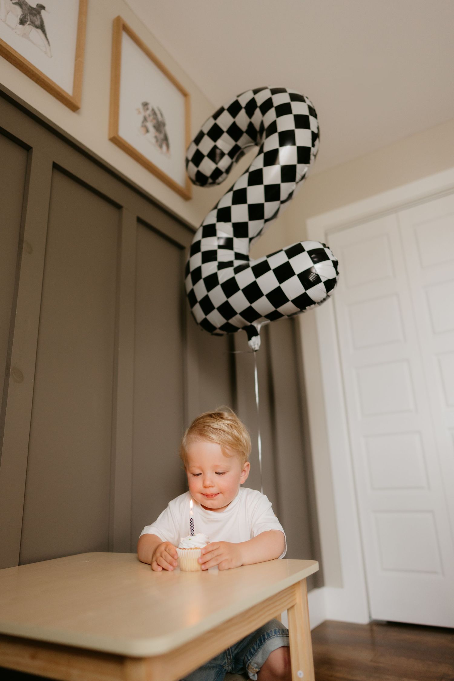 Toddler boy at wooden table with checkered number 2 balloon celebrating his 2nd birthday.