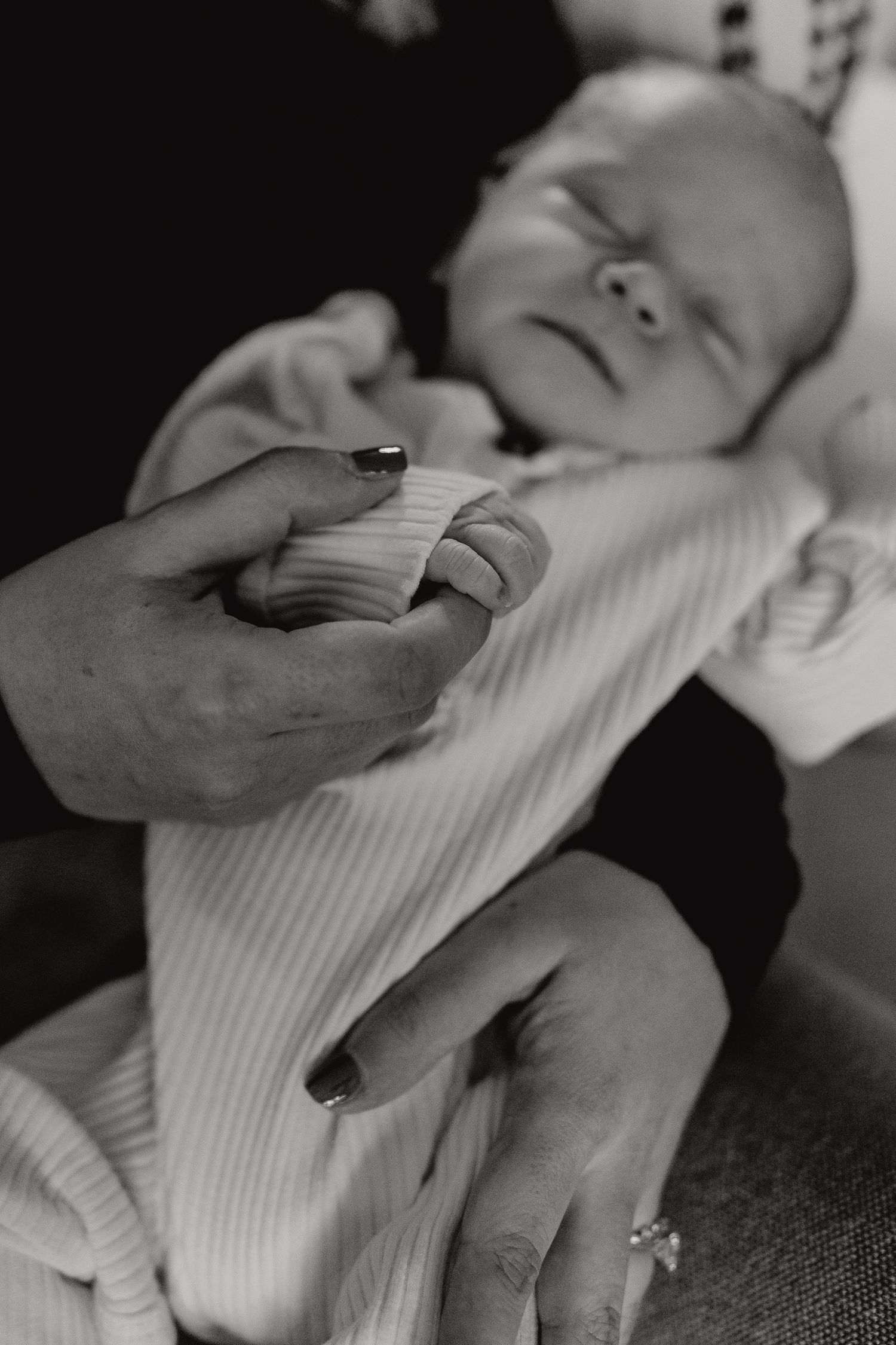 Black and white close-up of delicate hands touching a baby's ribbed white outfit.