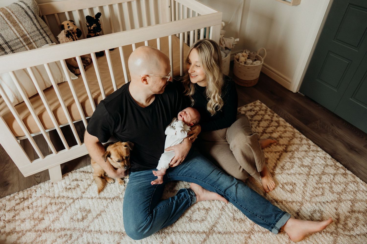 Family bonding moments on carpet floor next to white crib.
