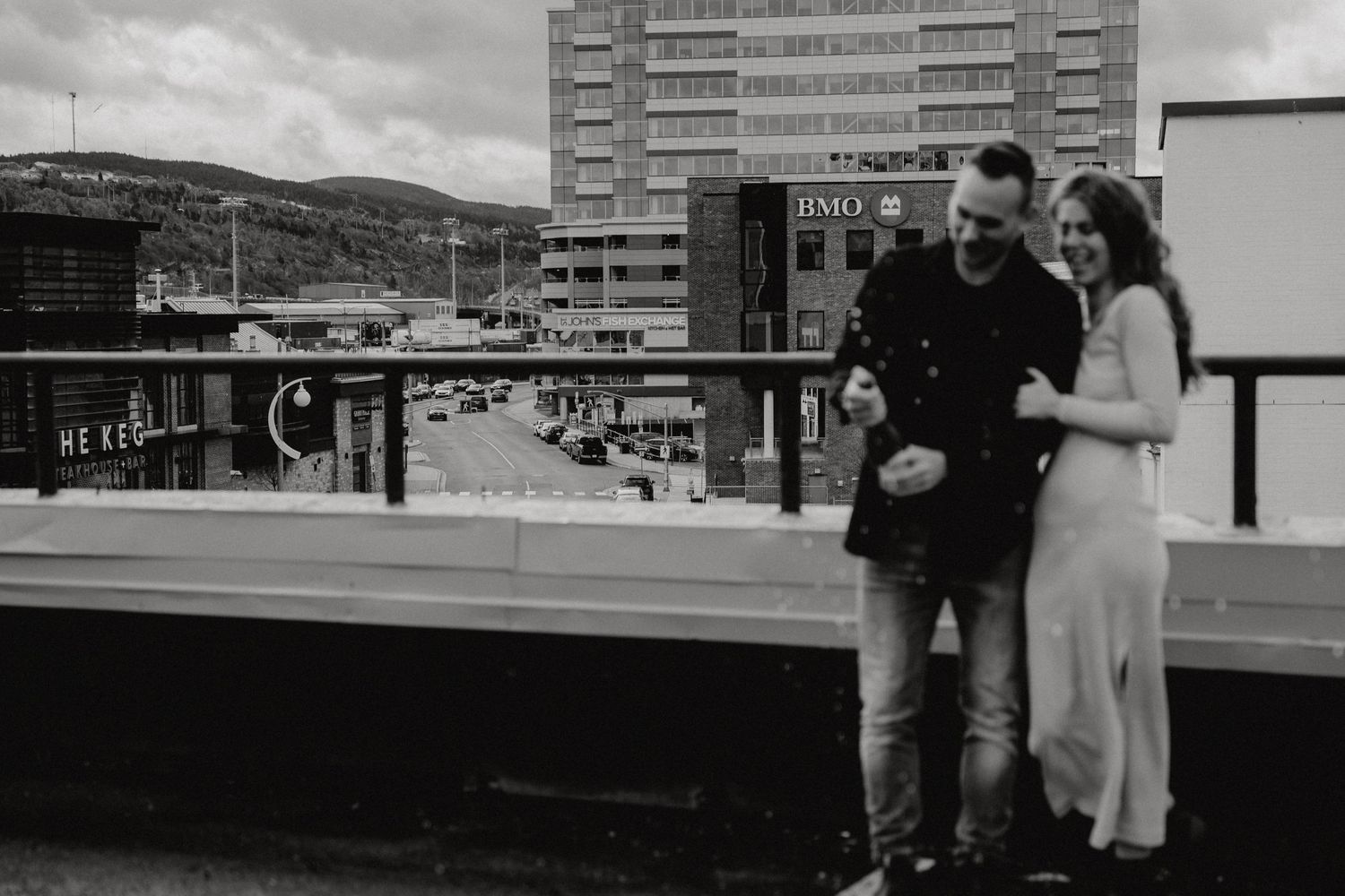 Two people share an intimate moment on a city rooftop with tall buildings in the background.