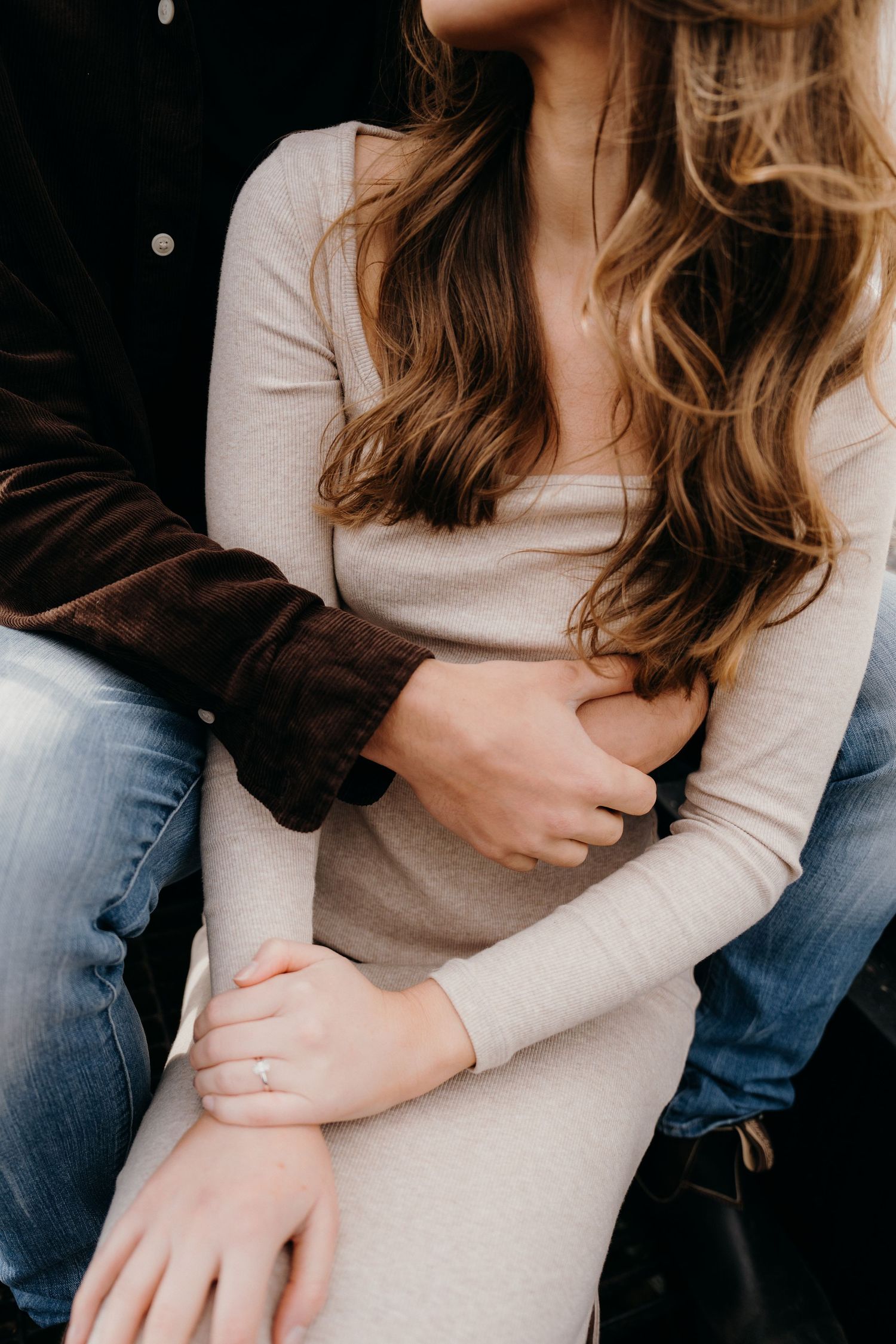Close-up details of couple embracing, wearing casual beige and black clothing.