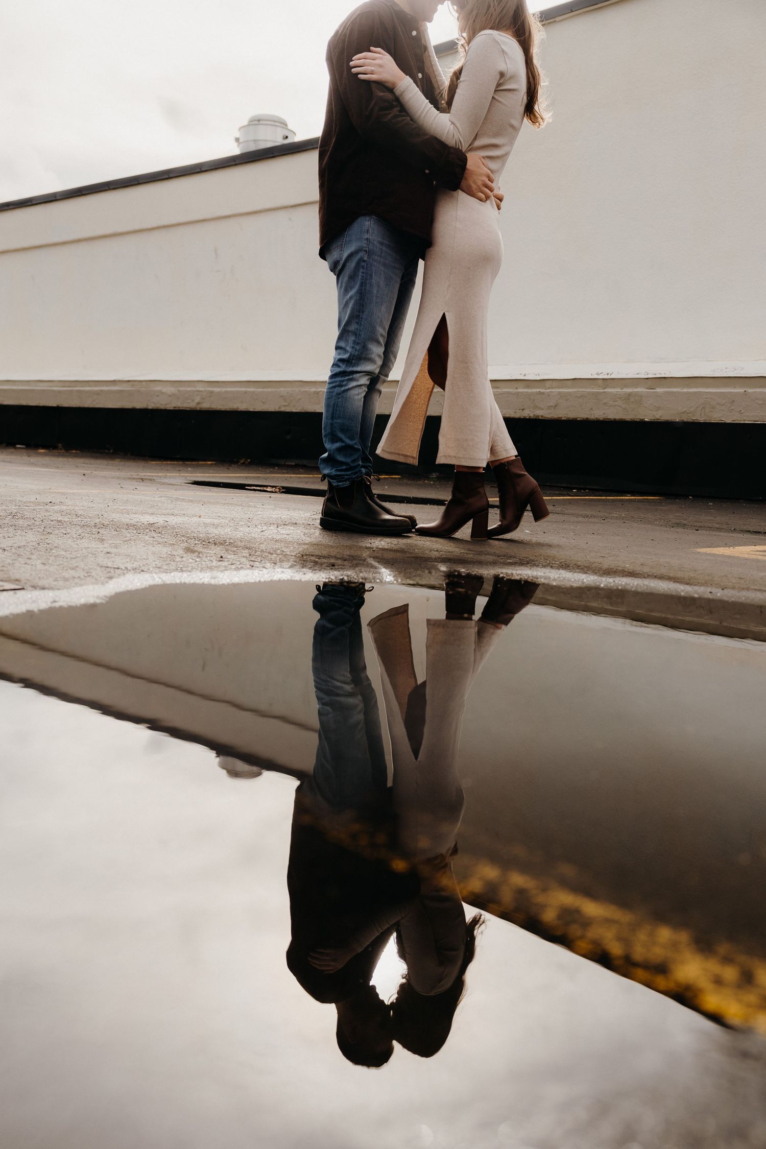 A romantic scene reflected in a puddle with industrial architecture creating strong lines.