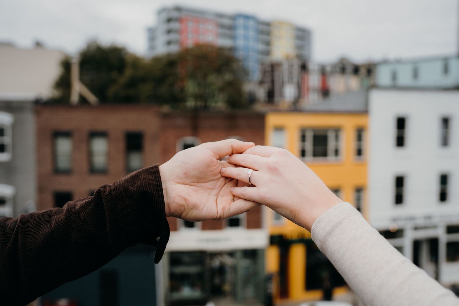 Reaching hands with engagement ring against cityscape backdrop.