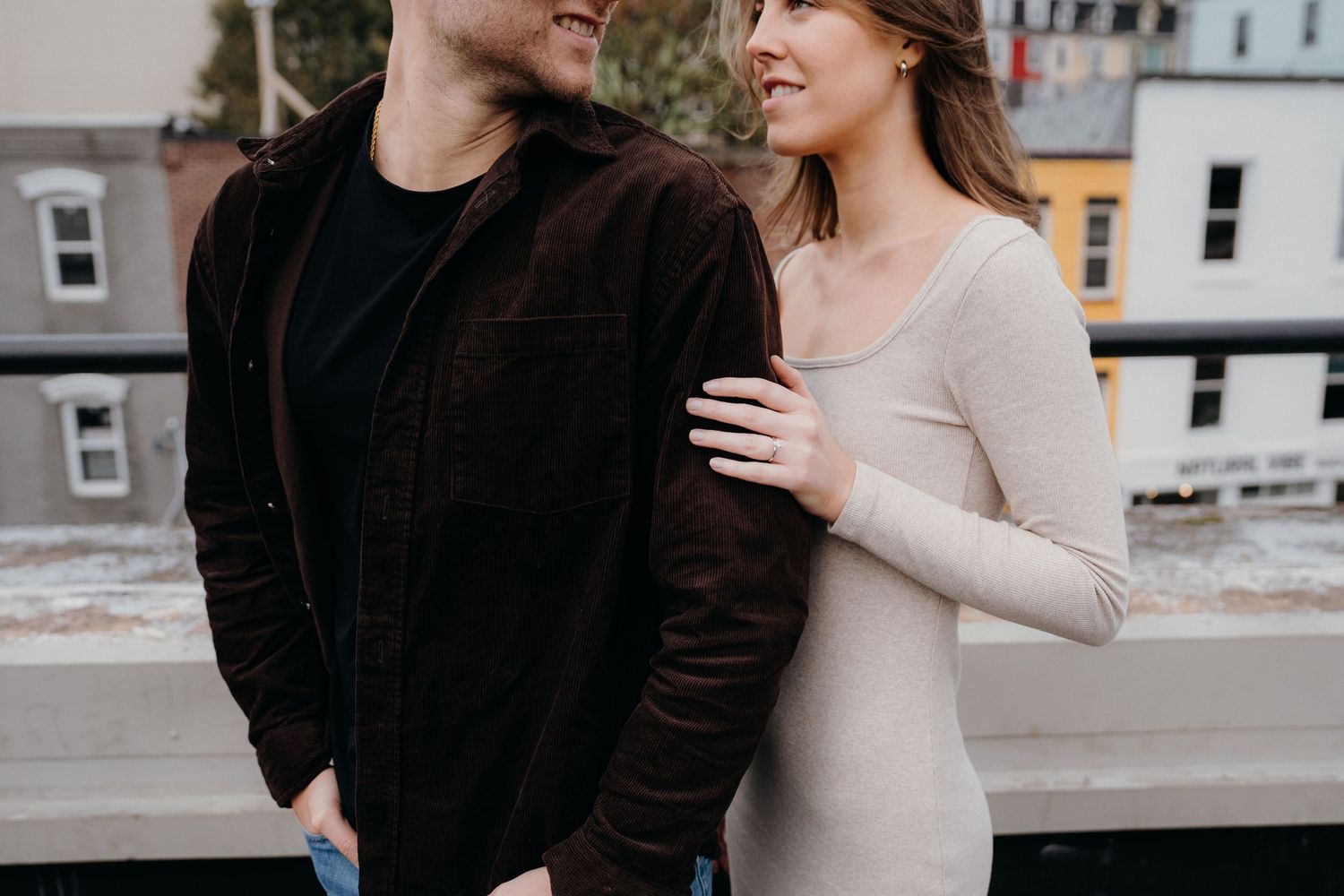 Couple smiling at each other during rooftop photo session with urban backdrop.