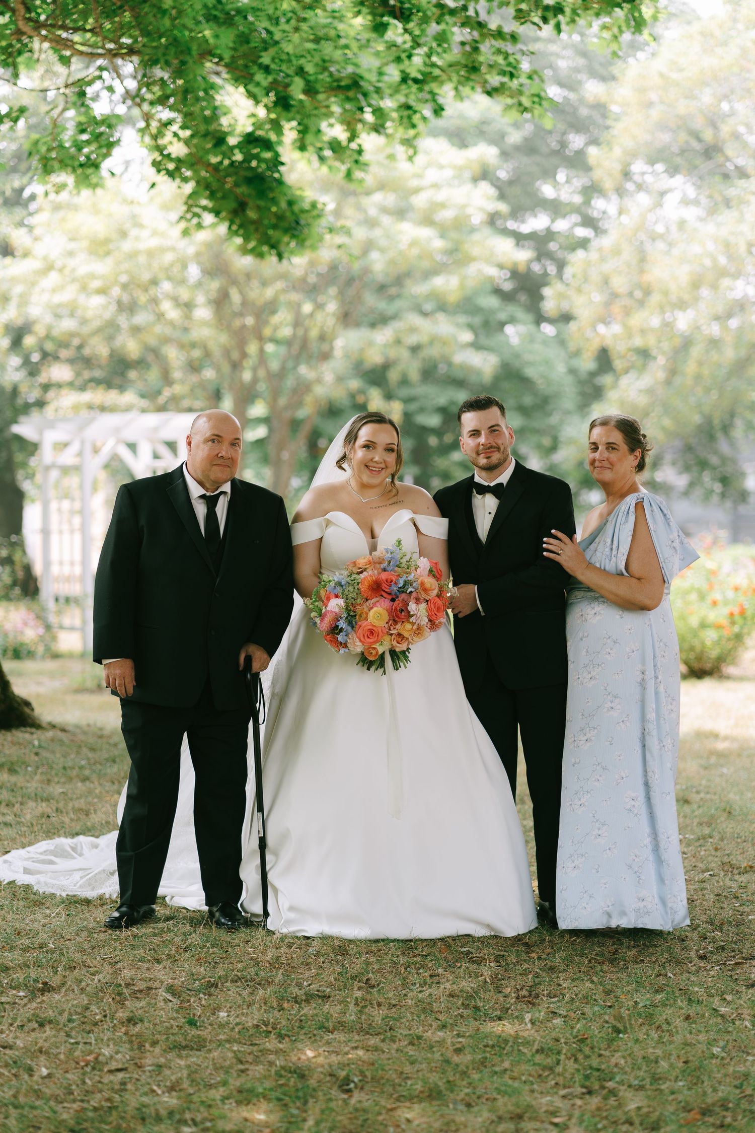 Wedding party posing for group photos on grassy lawn with colorful bouquet.