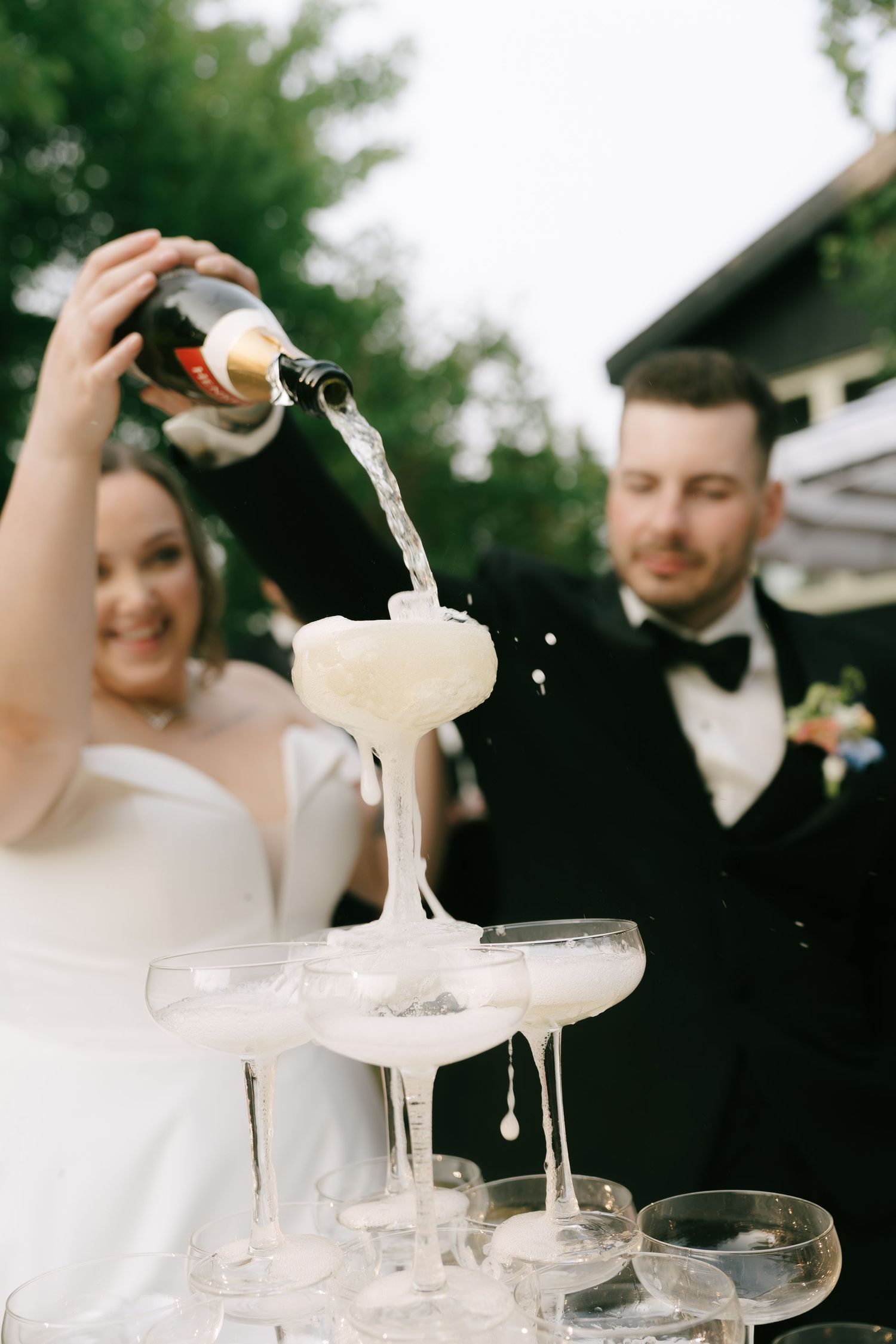 Wedding guests watch as champagne creates a sparkling waterfall effect through stacked crystal glasses.