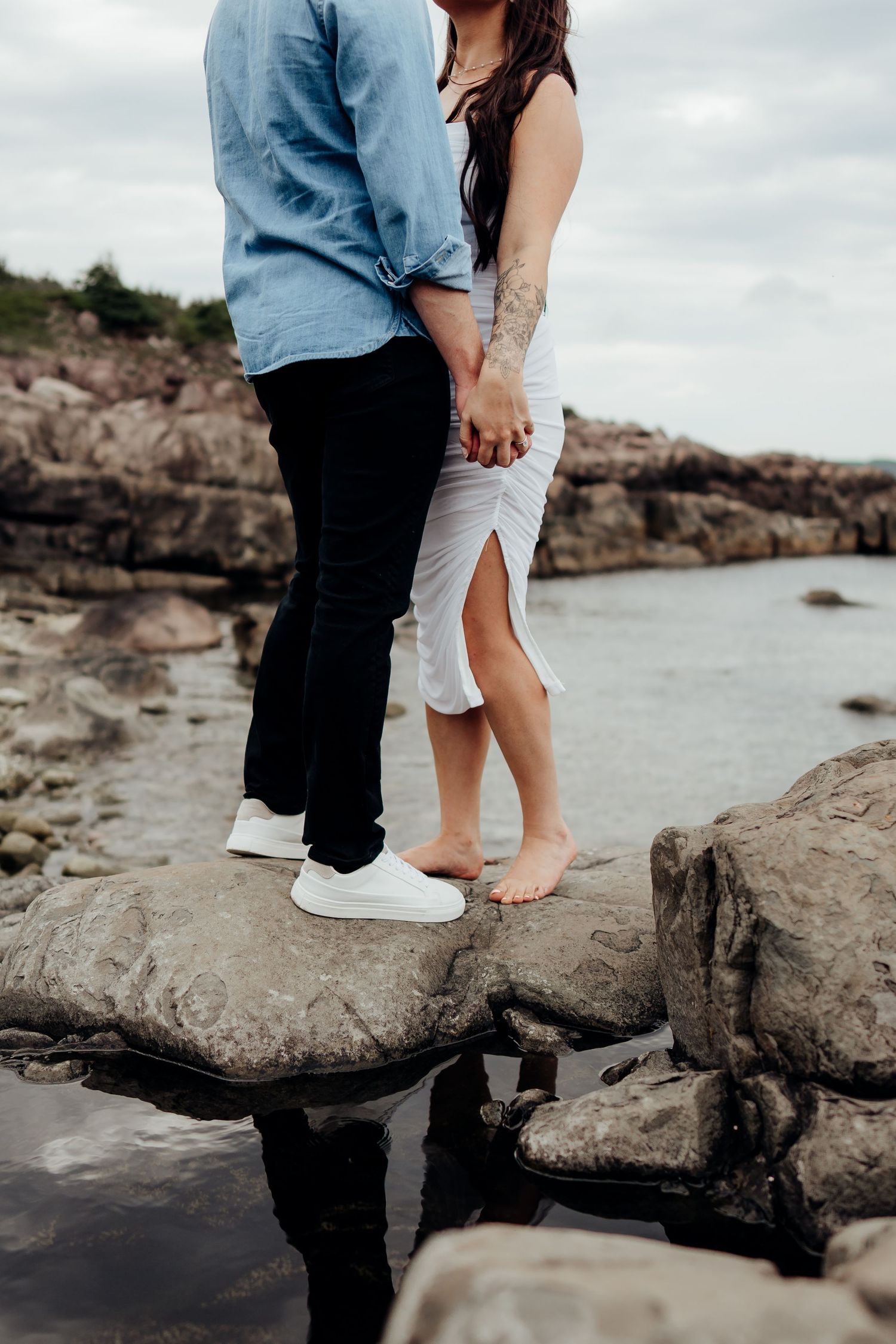Couple explores rocky beach shoreline together in casual attire.